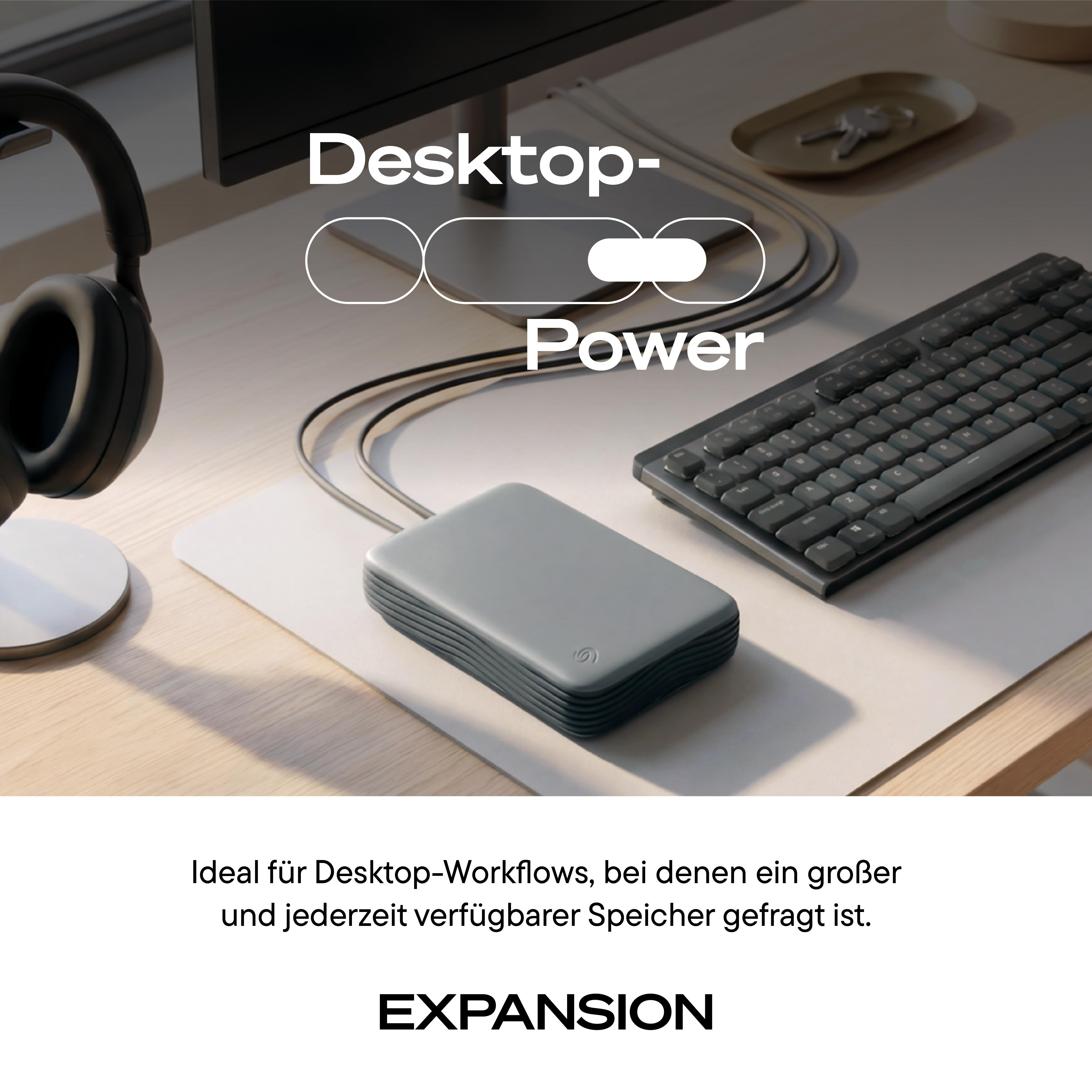 Graue externe Festplatte auf Schreibtisch mit Tastatur, Monitor und Kopfhörern.