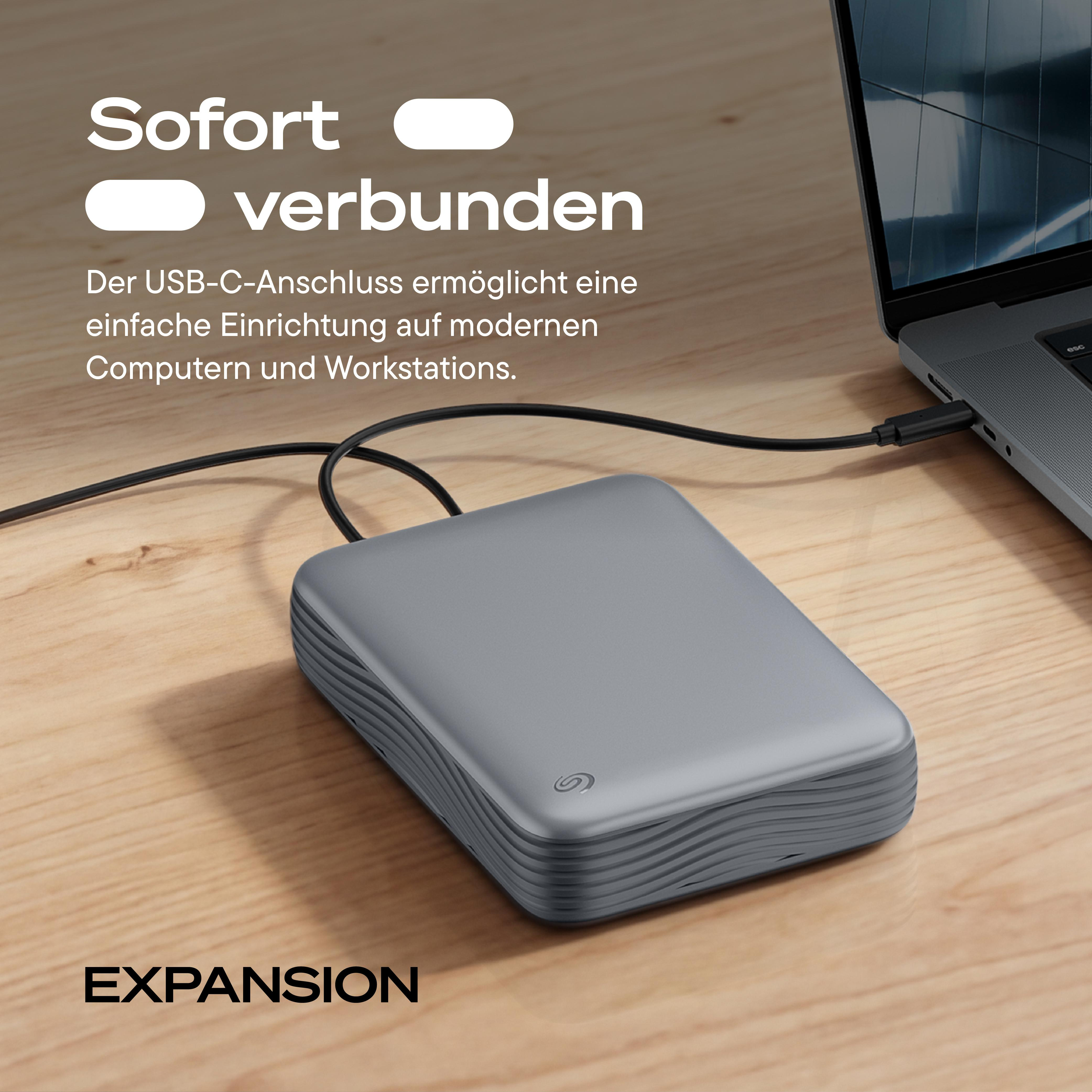 Eine graue externe Festplatte, per USB-C an ein Laptop auf einem Holztisch angeschlossen.