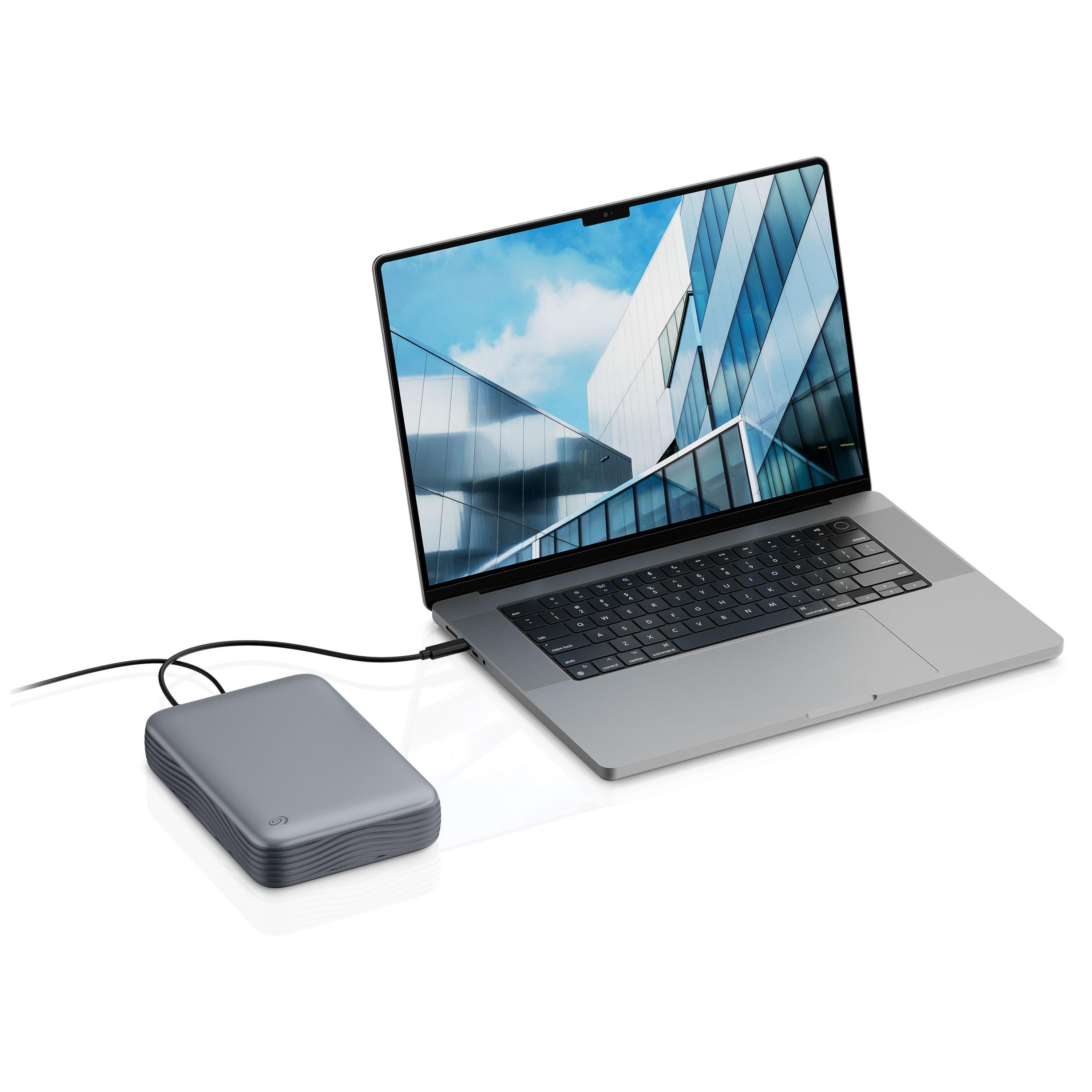 Eine graue externe Festplatte ist per Kabel mit einem modernen Laptop verbunden, der ein blaues Hintergrundbild zeigt.