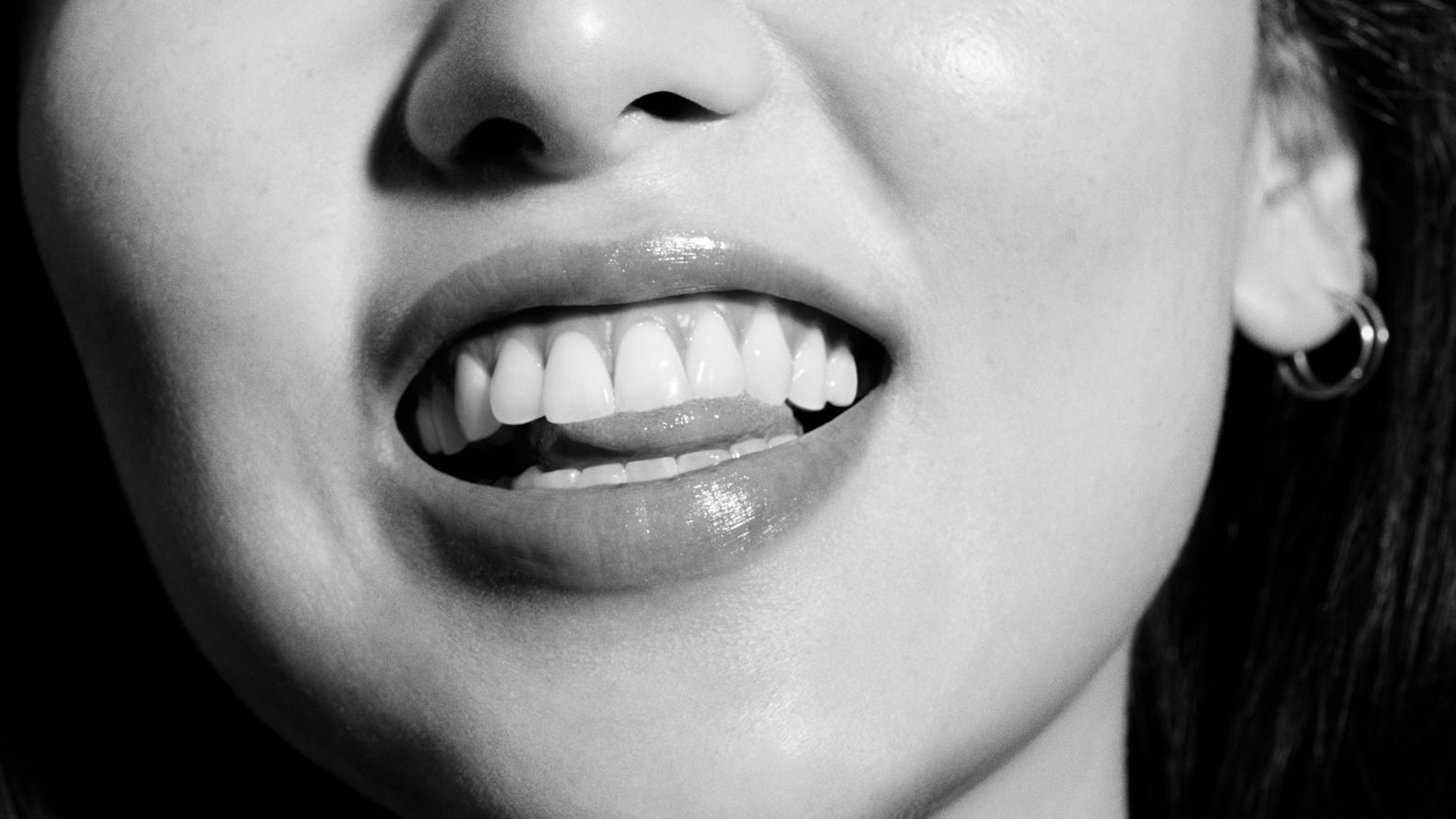 Gros plan en noir et blanc d'une femme souriante montrant des dents blanches et des lèvres brillantes.