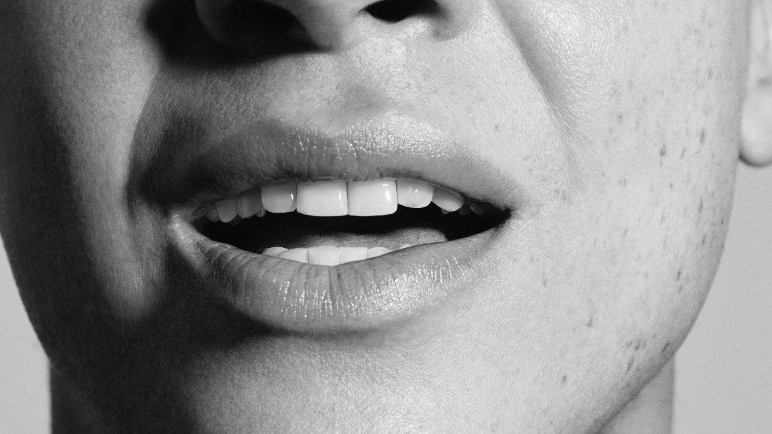 Gros plan sur la bouche souriante et les dents d'une personne en noir et blanc.