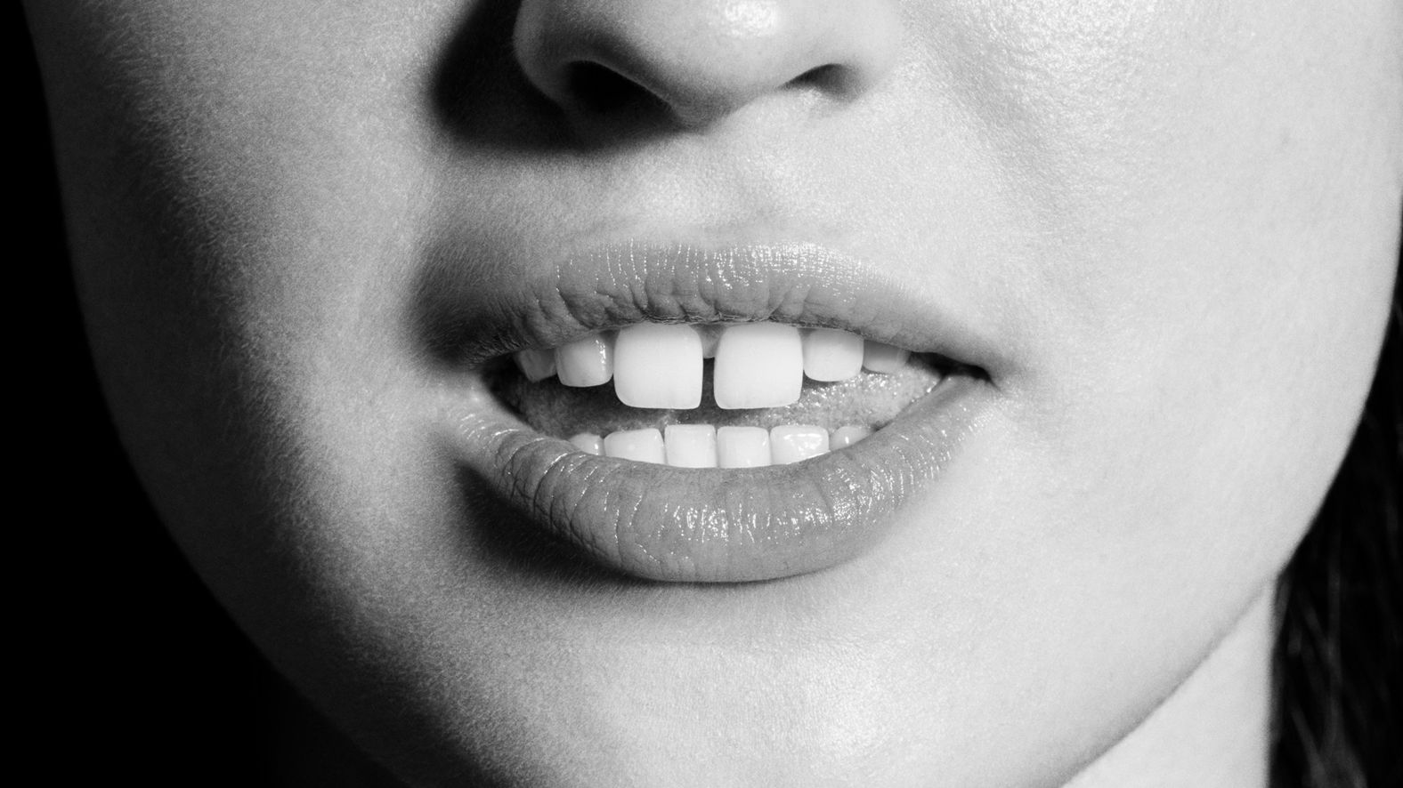 Gros plan en noir et blanc du nez et des lèvres d'une femme, montrant des dents avec un espace.