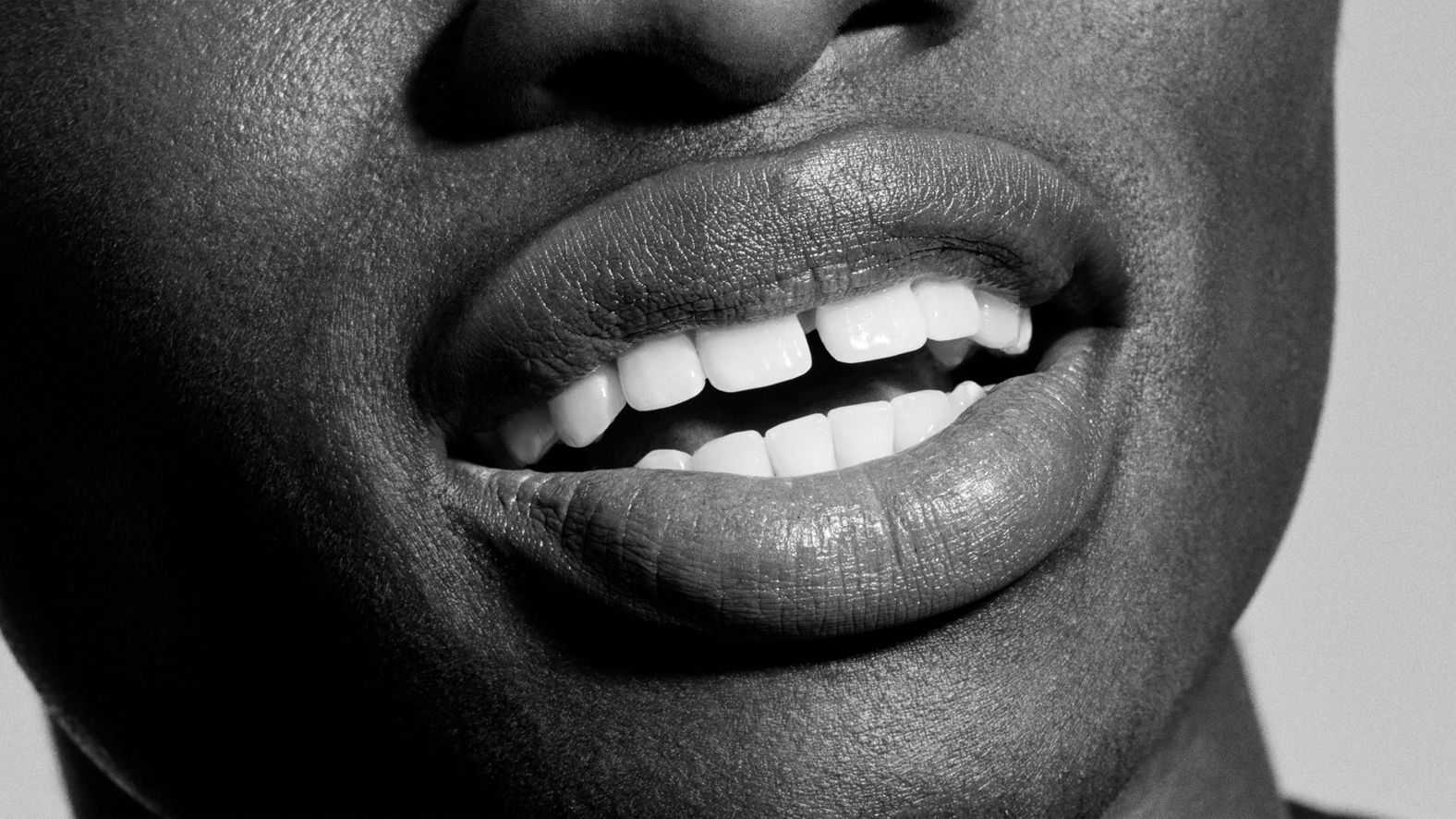 Gros plan en noir et blanc d'une personne souriant, montrant des dents blanches et un petit espace.