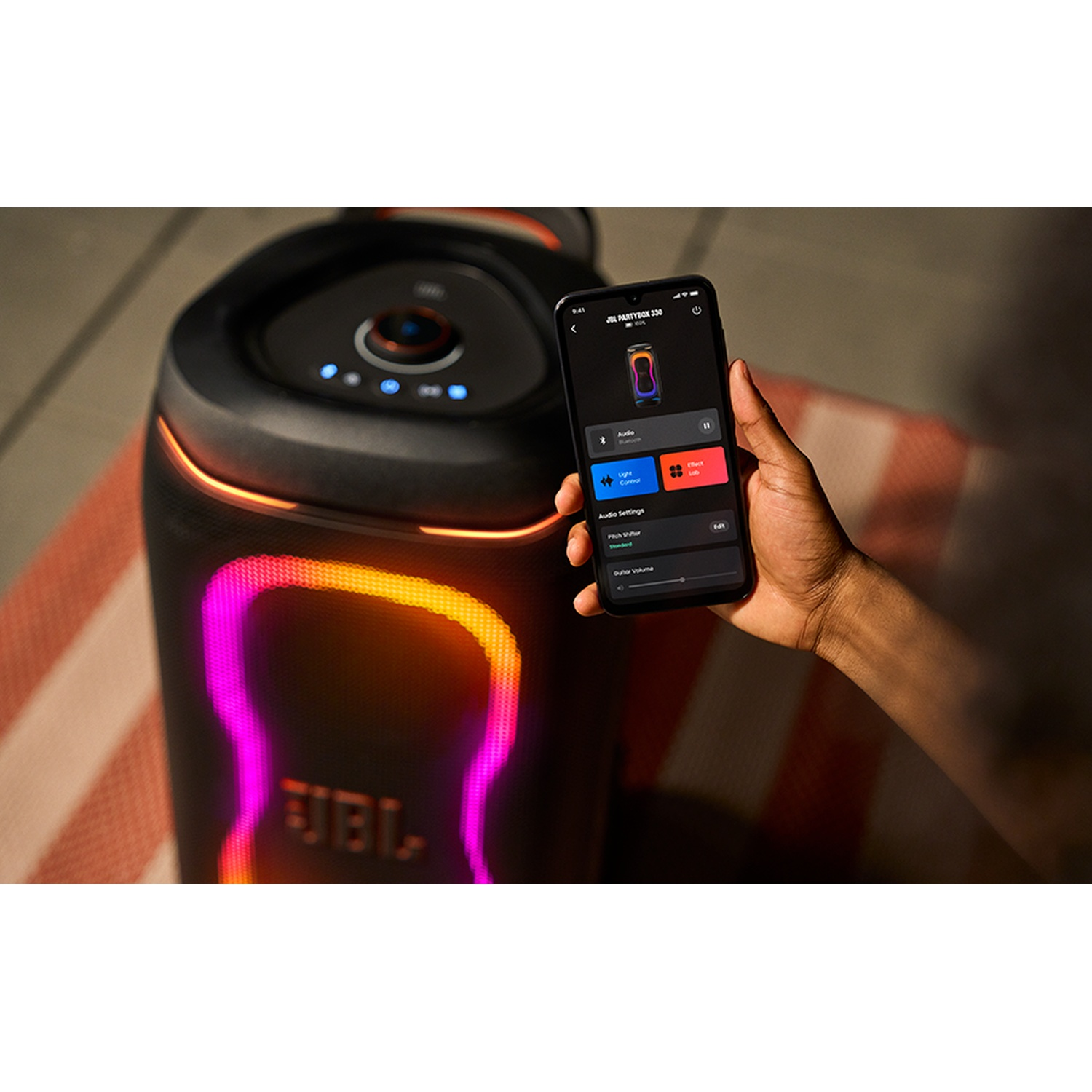 A smartphone controls a large JBL party speaker with colorful lights.