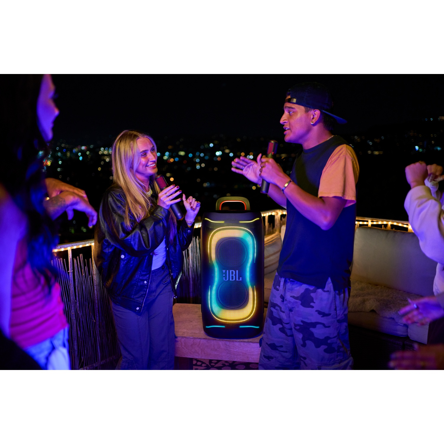 Friends sing outdoors at night in front of an illuminated JBL speaker.
