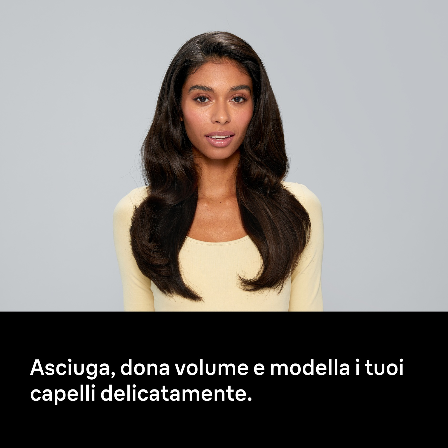 Una donna con lunghi capelli scuri e top giallo su sfondo grigio, con testo in basso.