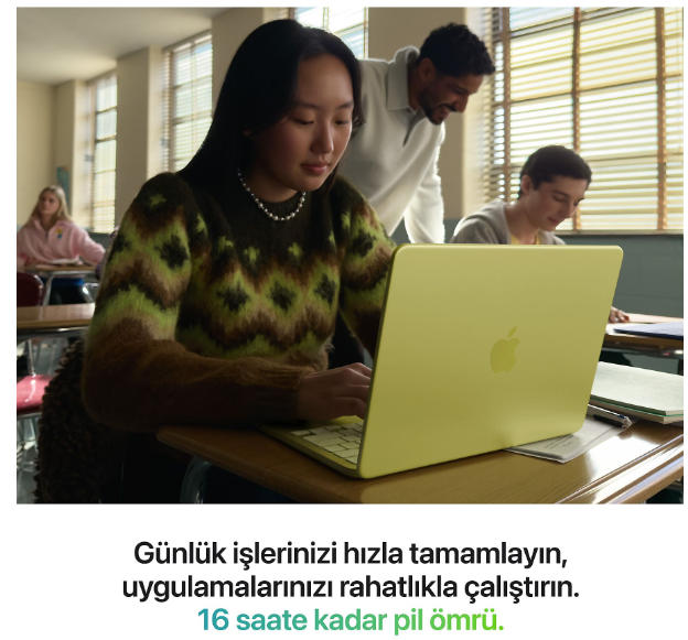 Bir kız öğrenci sınıfta sarı bir dizüstü bilgisayar kullanıyor, arka planda öğretmen ve öğrenciler var.