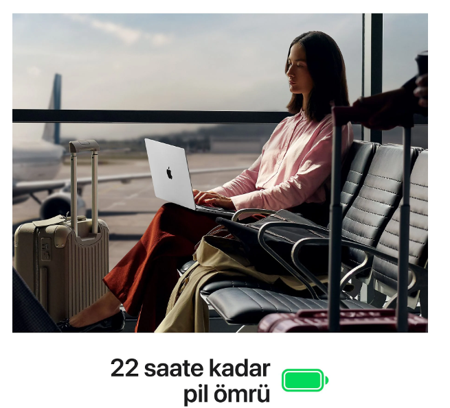 Havaalanı kapısında oturan bir kadın arka planda uçak ve bavullarla dizüstü bilgisayar kullanıyor.