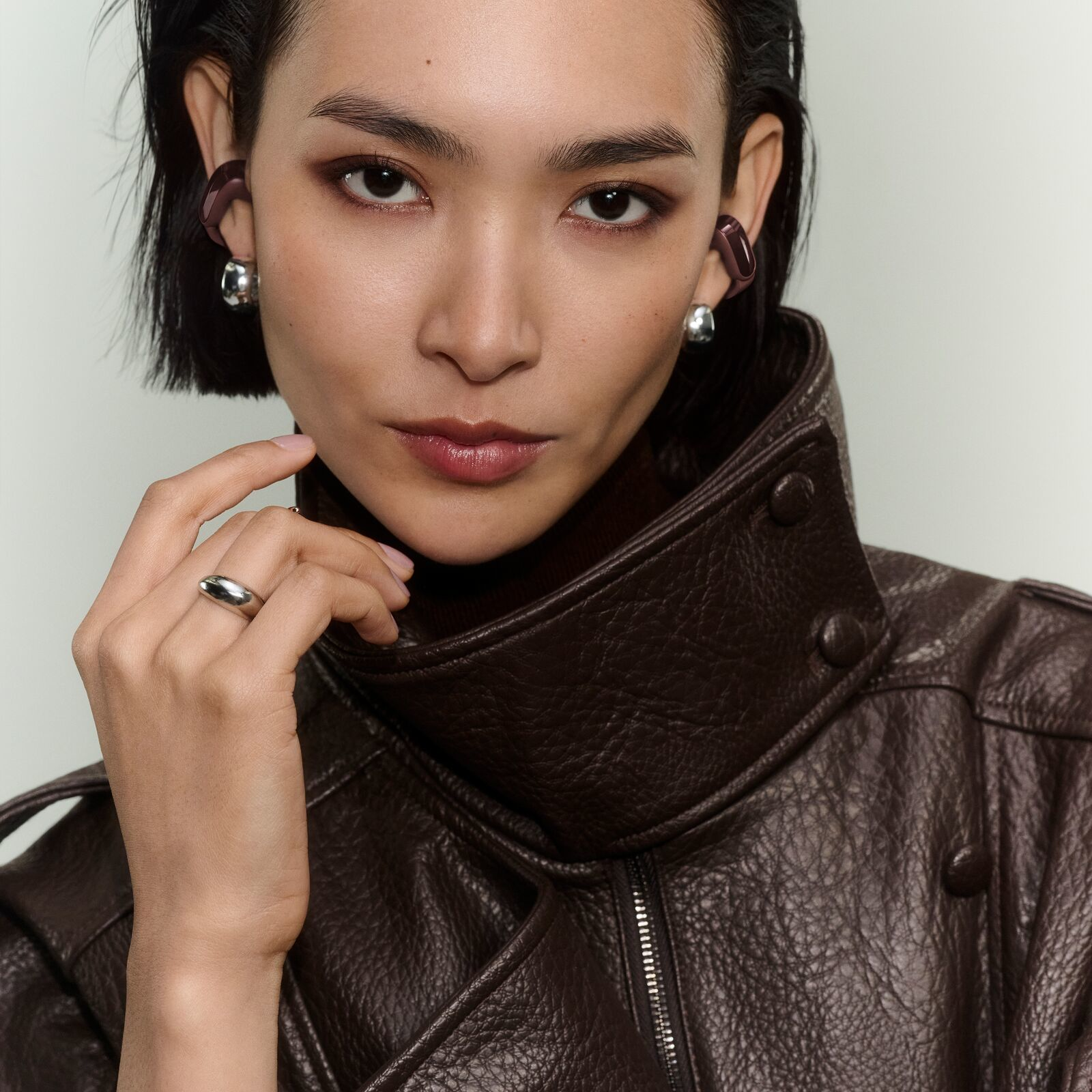 Eine asiatische Frau mit schwarzem Haar trägt eine braune Lederjacke und Ohrhörer.