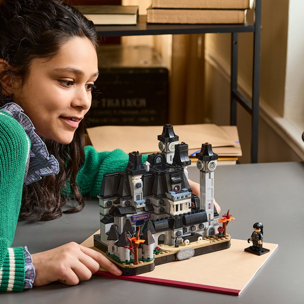 Ein junges Mädchen in grünem Pulver betrachtet lächelnd ein fertiges Lego-Schlossmodell auf einem Tisch.