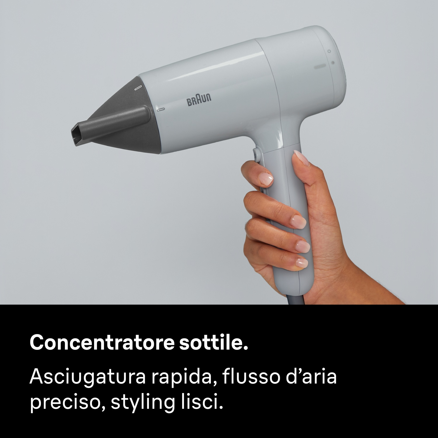Una mano regge un asciugacapelli Braun grigio chiaro con bocchetta scura su sfondo neutro.