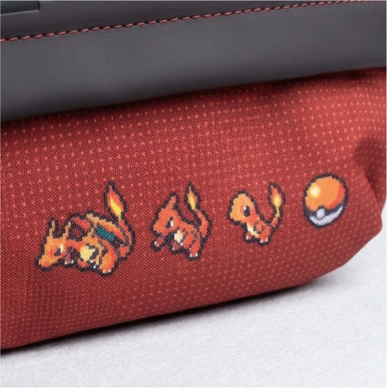 Tessuto rosso con Pokémon pixel e Pokéball stampati, sotto un bordo nero.