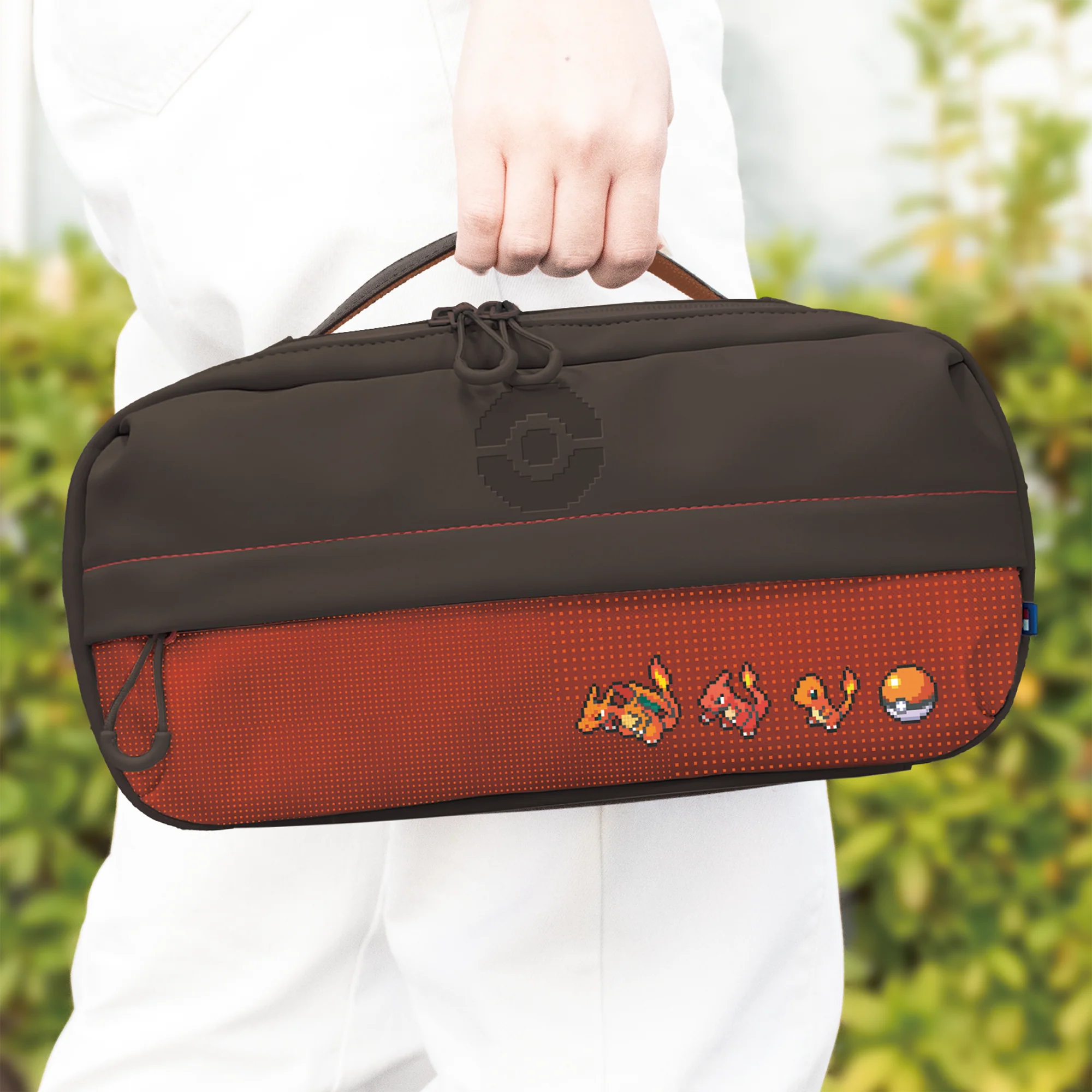 Una persona tiene in mano una borsa Pokemon marrone e rossa con grafica pixel di Charizard.