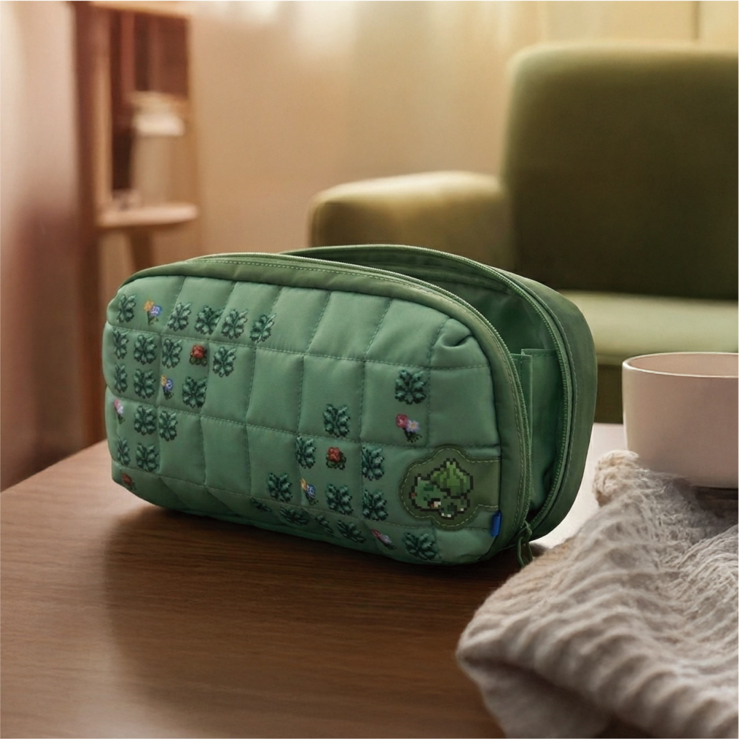Un beauty case verde trapuntato con ricami poggia su un tavolo di legno, con una poltrona sullo sfondo.