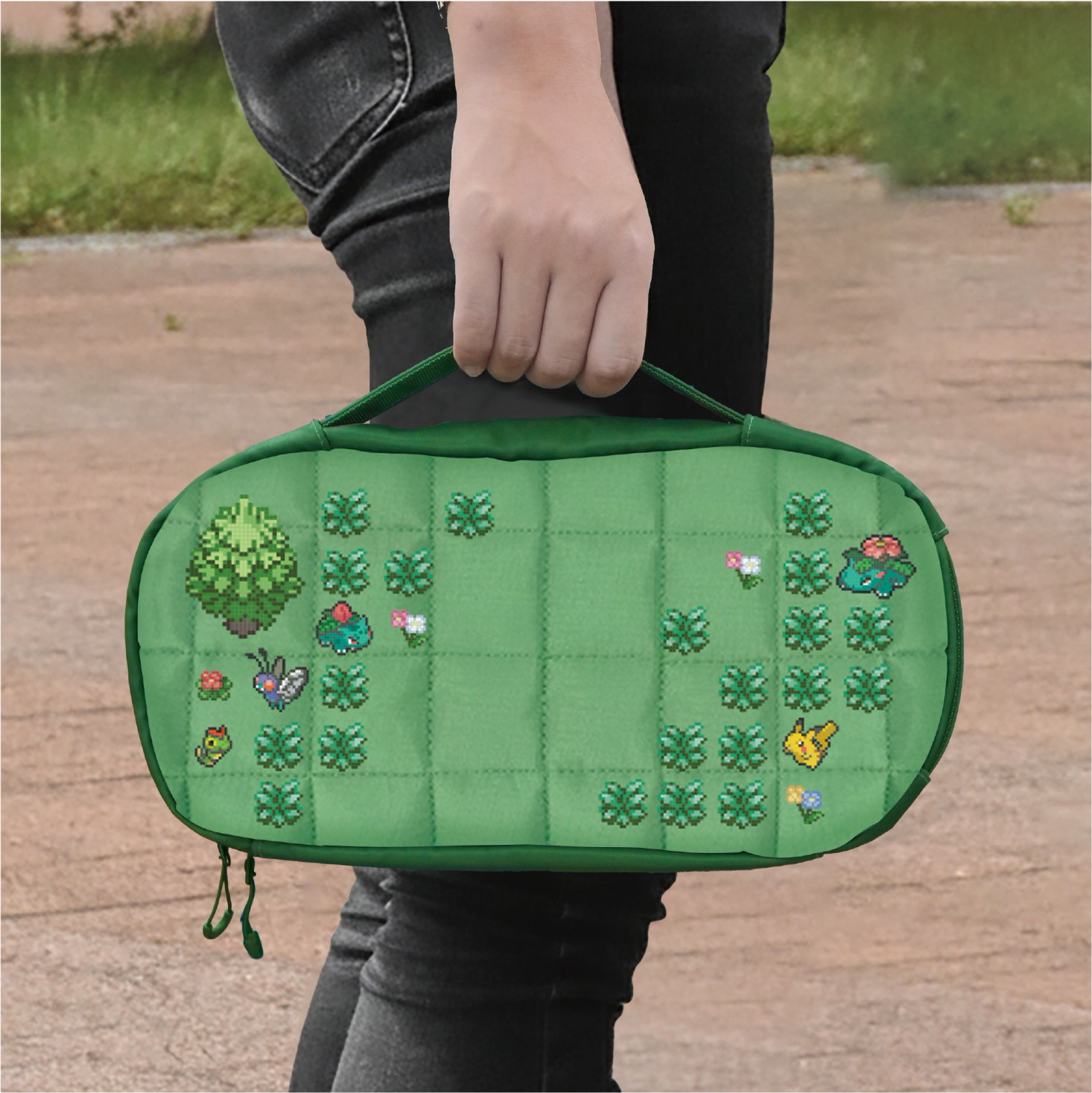 Persona che tiene una borsa verde con motivi in pixel art di Pokémon retro, alberi ed erba.
