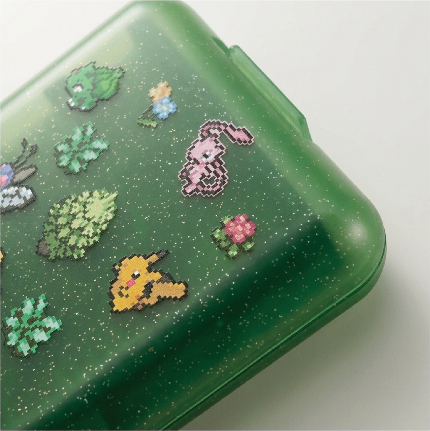 Custodia verde traslucida glitterata decorata con adesivi in pixel art di personaggi Pokémon su sfondo bianco.