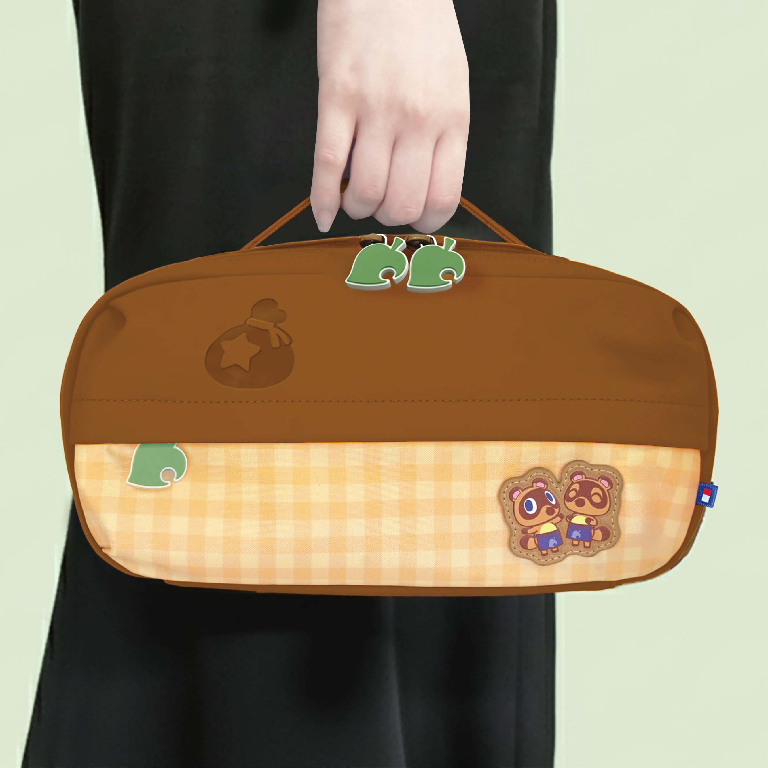 Persona in nero regge una borsa marrone di Animal Crossing con motivo a quadri e personaggi.
