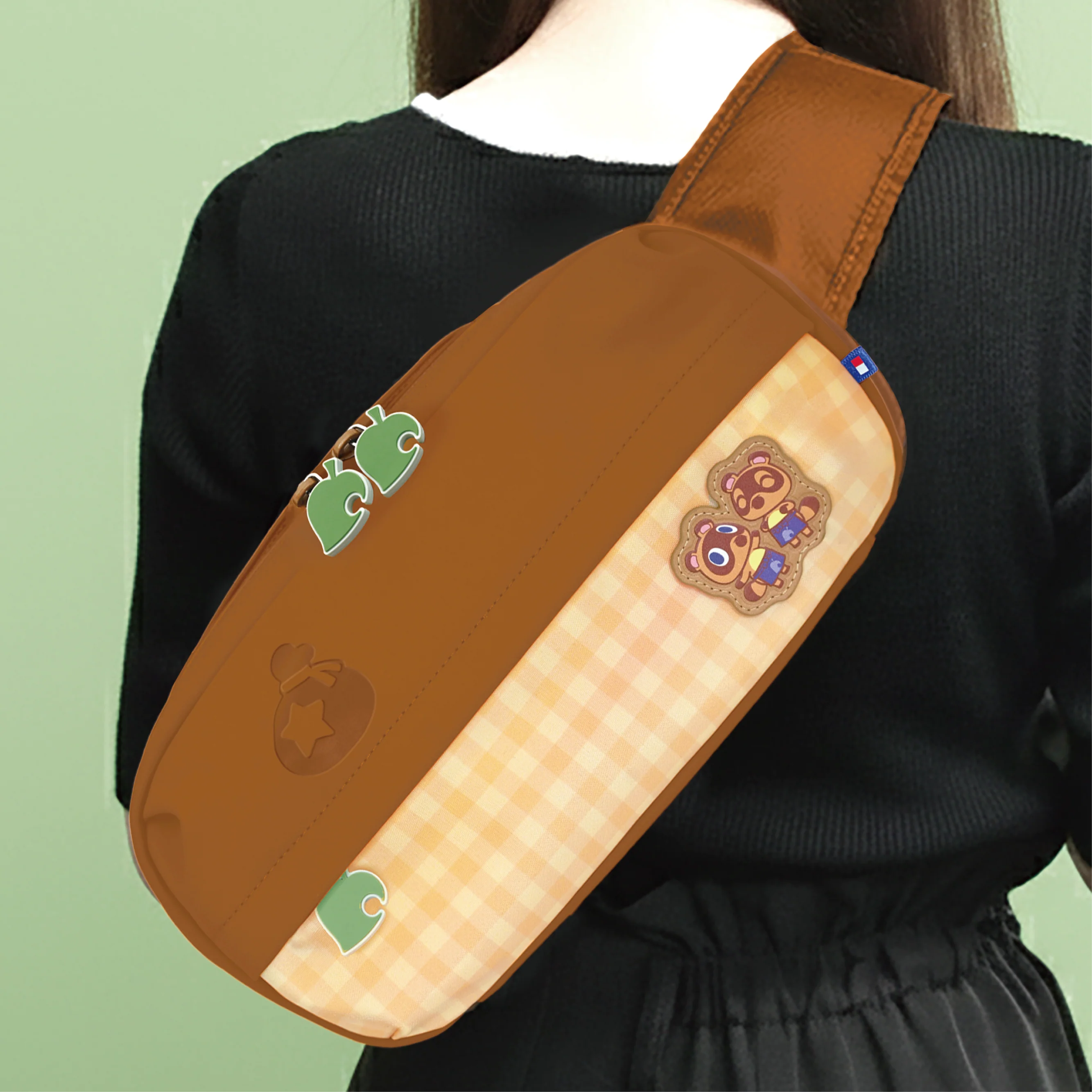 Una borsa a tracolla marrone con motivo a quadri, personaggi animali e cursori a foglia su sfondo verde.