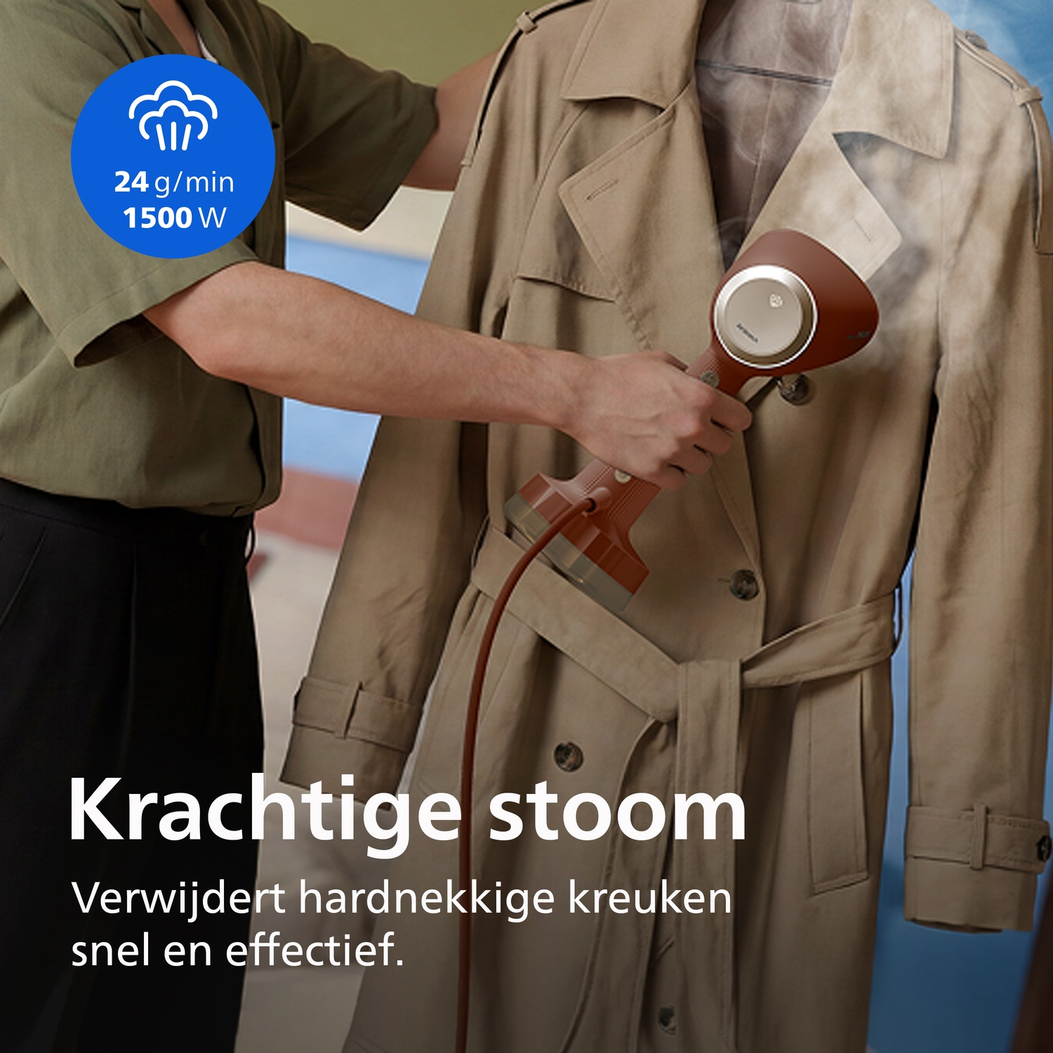 Person steaming a beige trench coat with a red hand steamer.