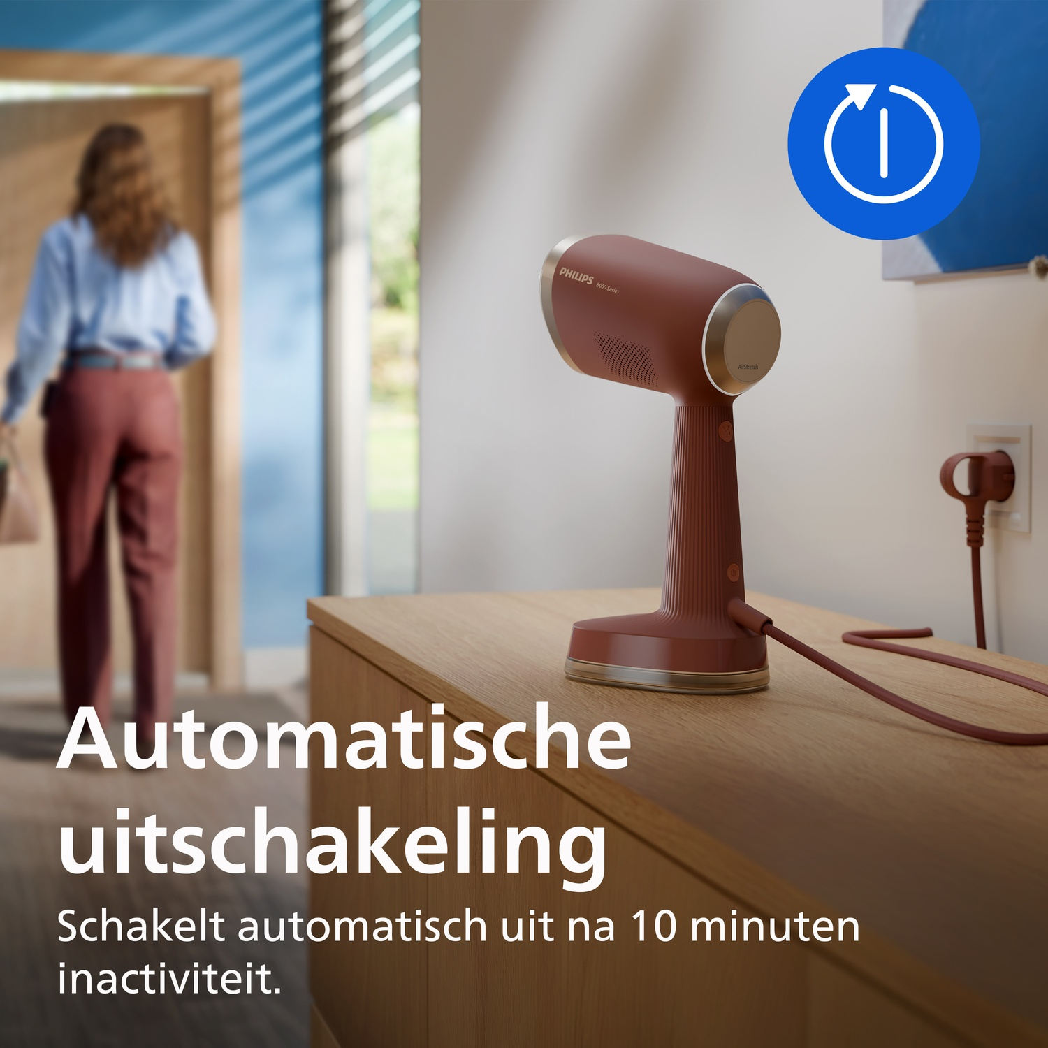 Red Philips garment steamer on wooden table in modern room, woman in background, blue circle with white icon.