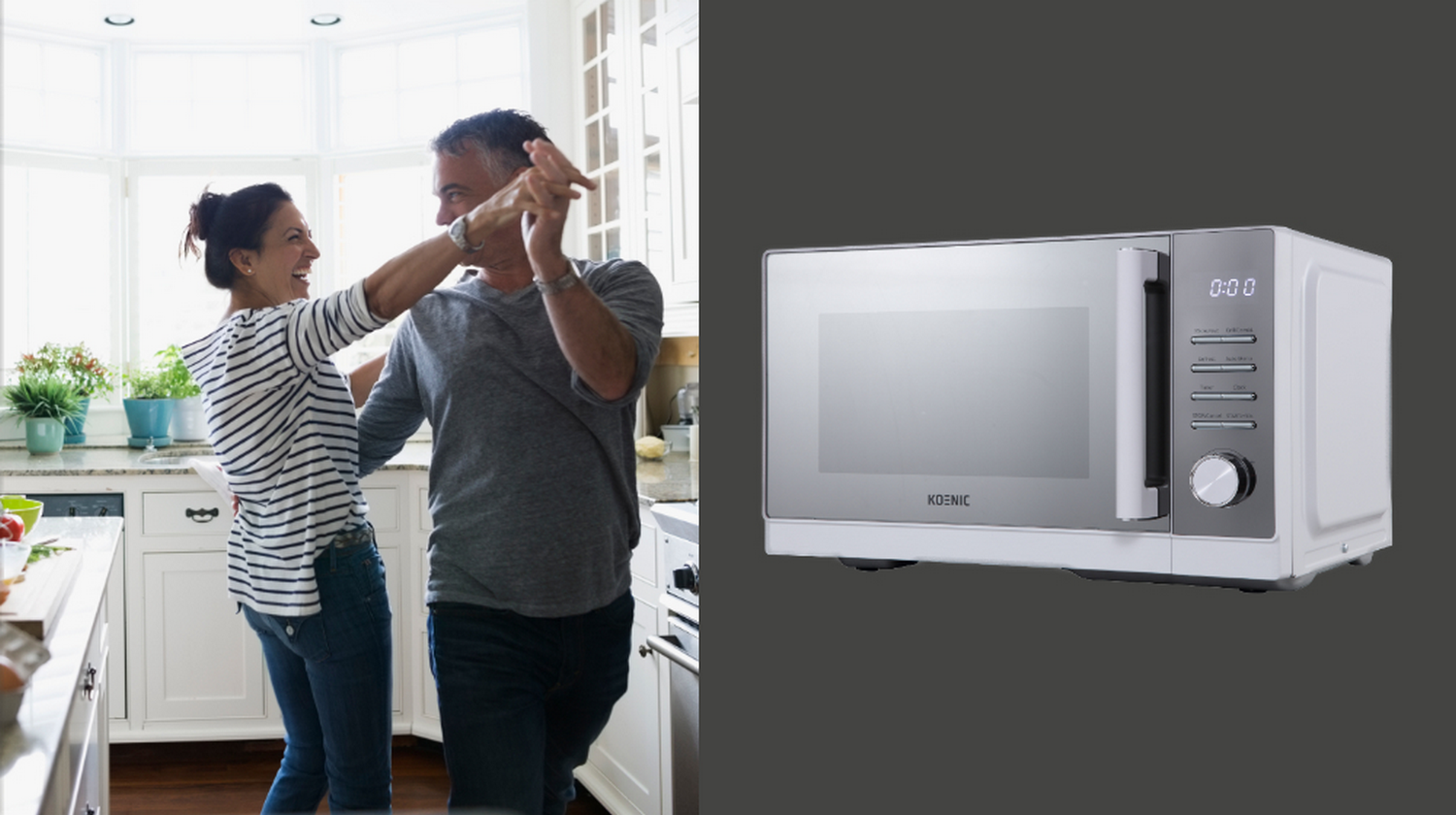 Una pareja feliz baila en una cocina luminosa junto a un horno microondas de acero inoxidable.