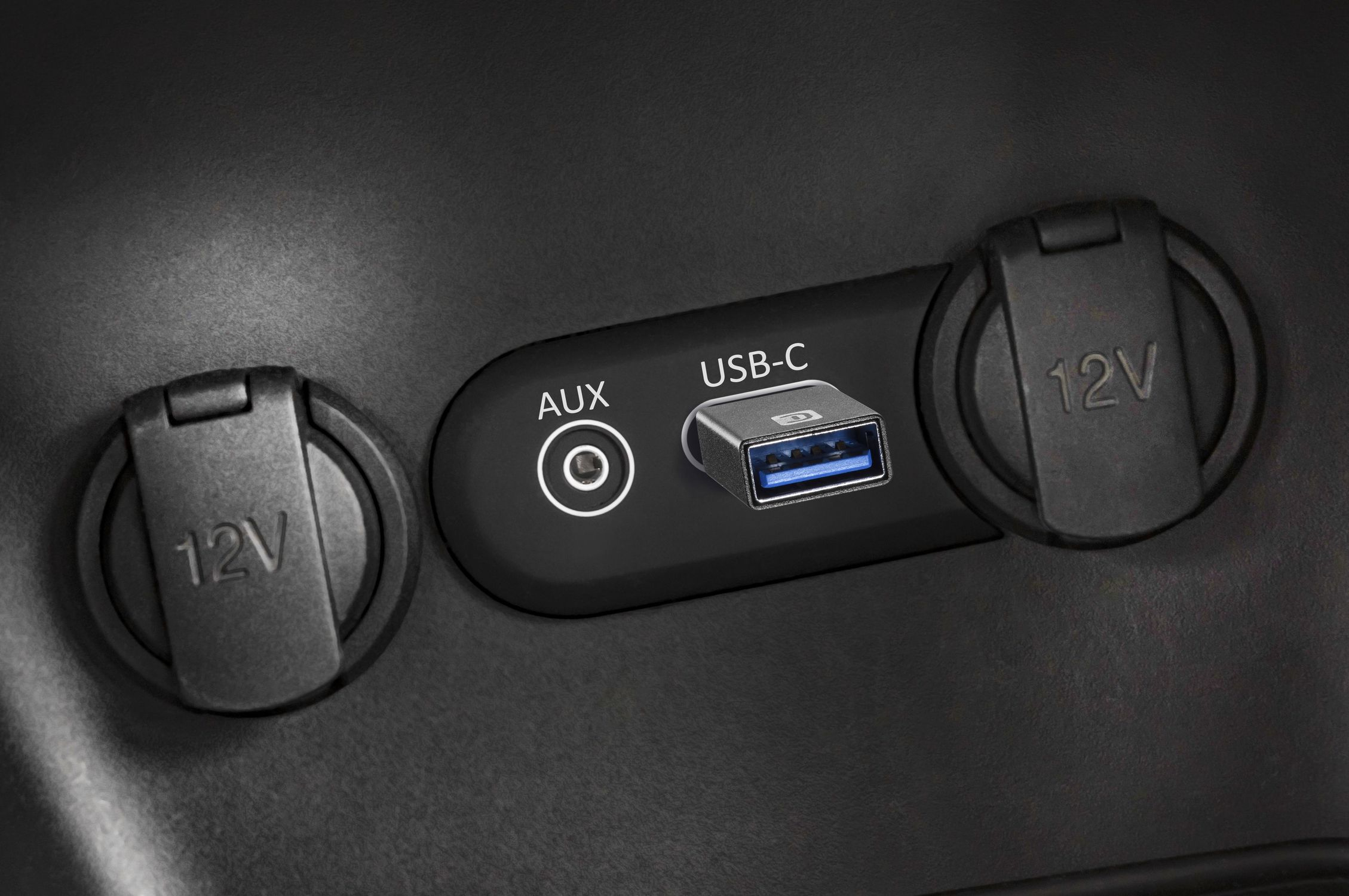 Primer plano de puertos de coche: dos enchufes de 12V, un puerto AUX y una conexión USB-C.