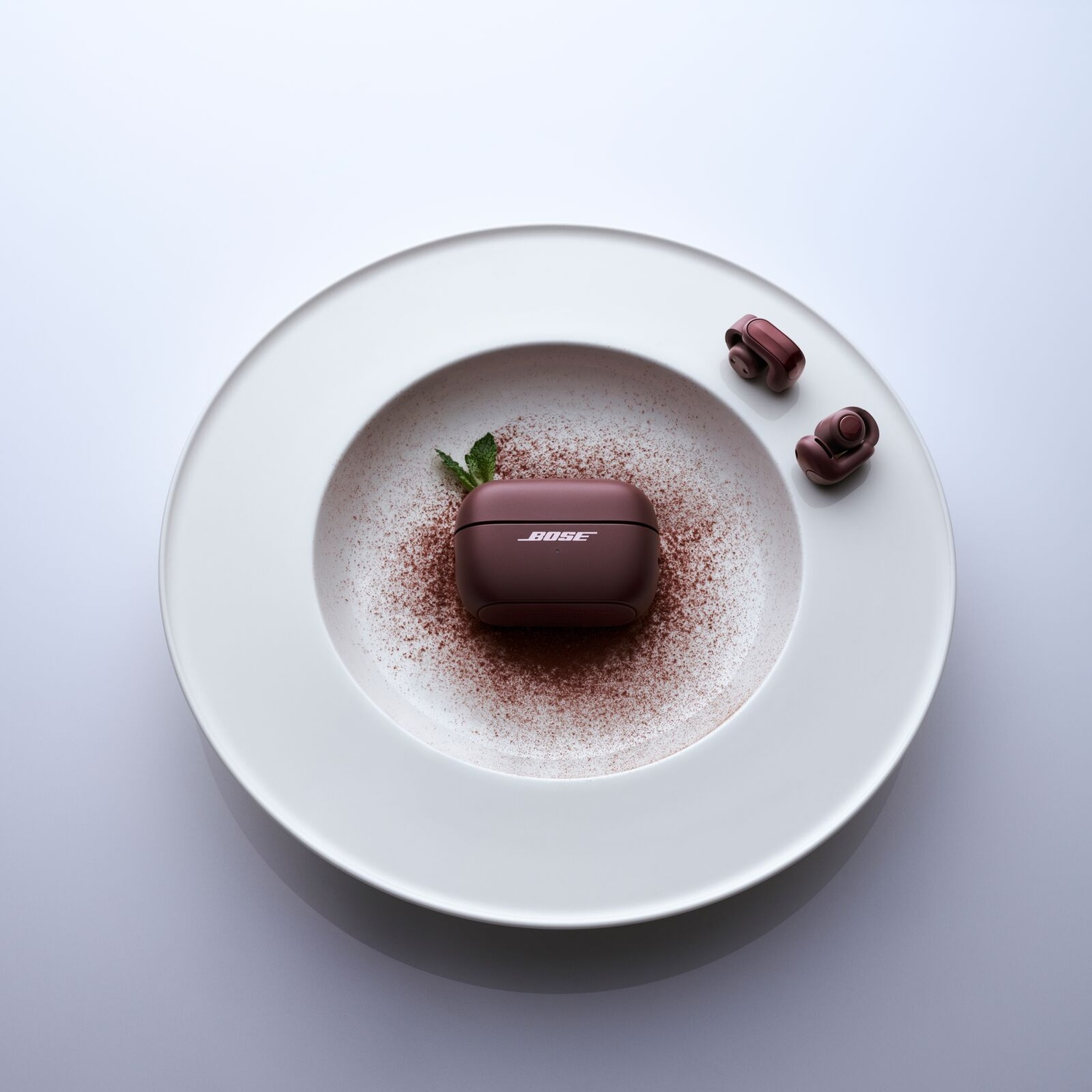 Bose oordopjes en oplaadcase in een witte kom met cacaopoeder en munt.