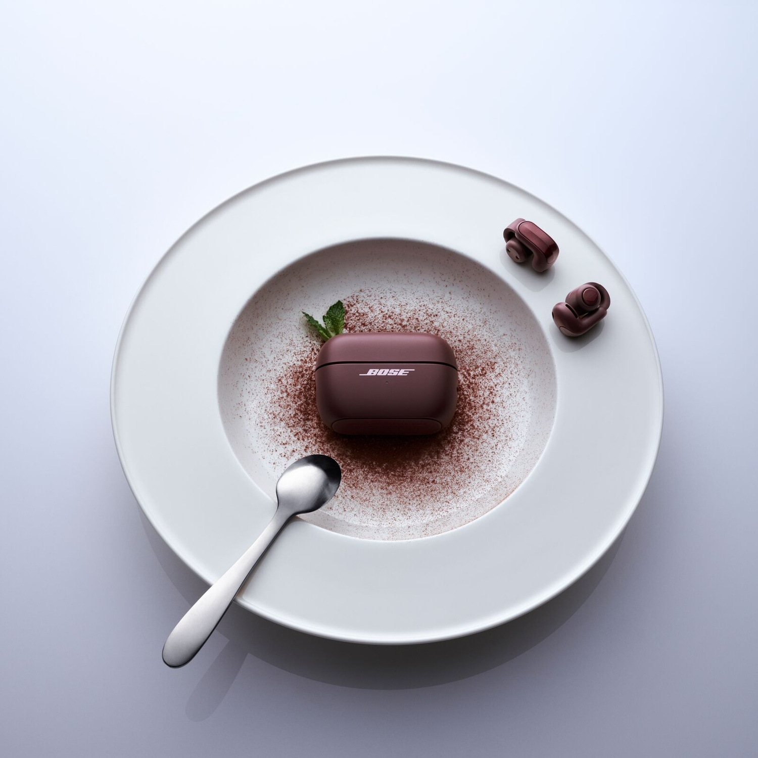 Bose-oordopjes in een witte schaal met cacaopoeder, munt en een lepel.