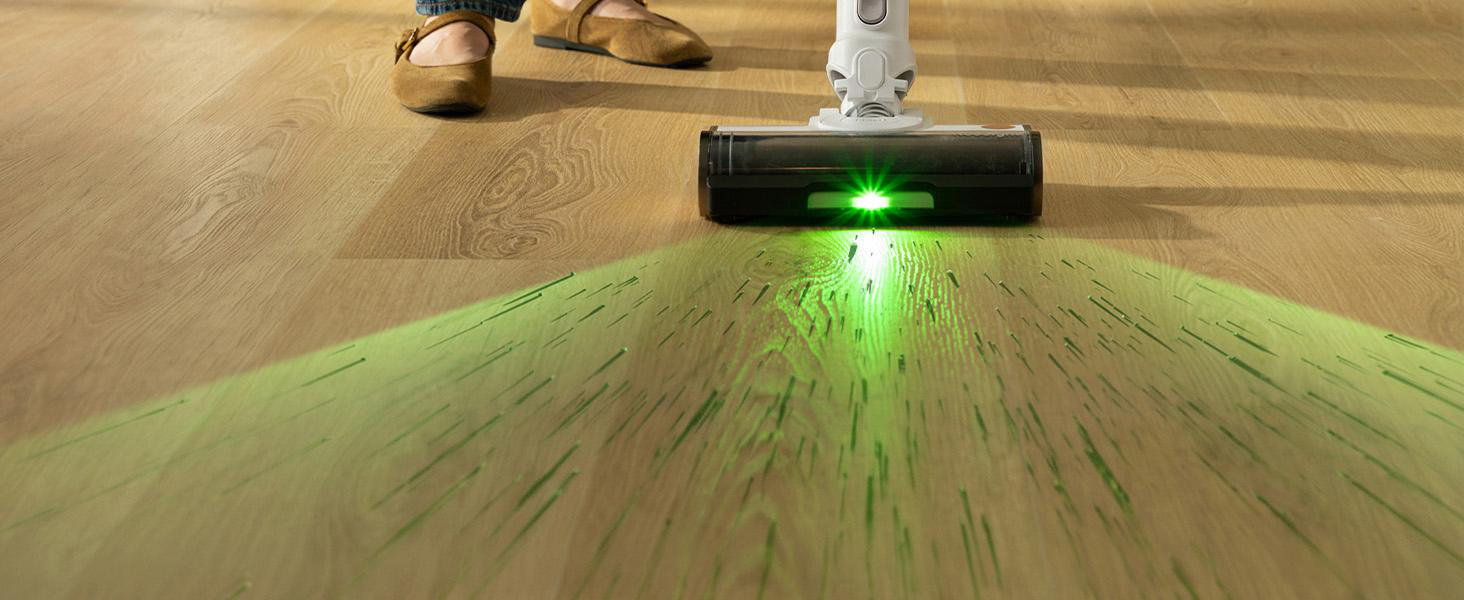 Ein Staubsauger mit grünem Laserlicht leuchtet den Holzboden aus, während eine Person im Hintergrund steht.