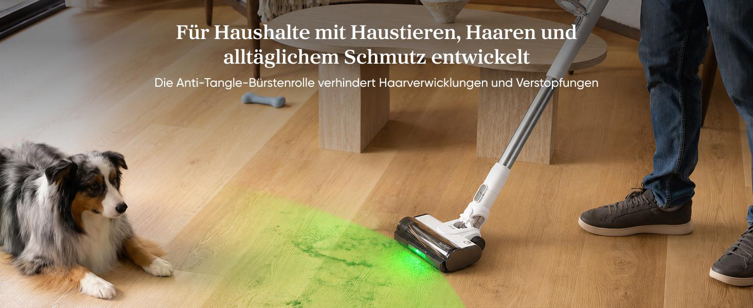 Ein Staubsauger mit Grünlicht reinigt einen Holzfußboden in einem Wohnzimmer neben einem Hund und einer Kaffeetisch.