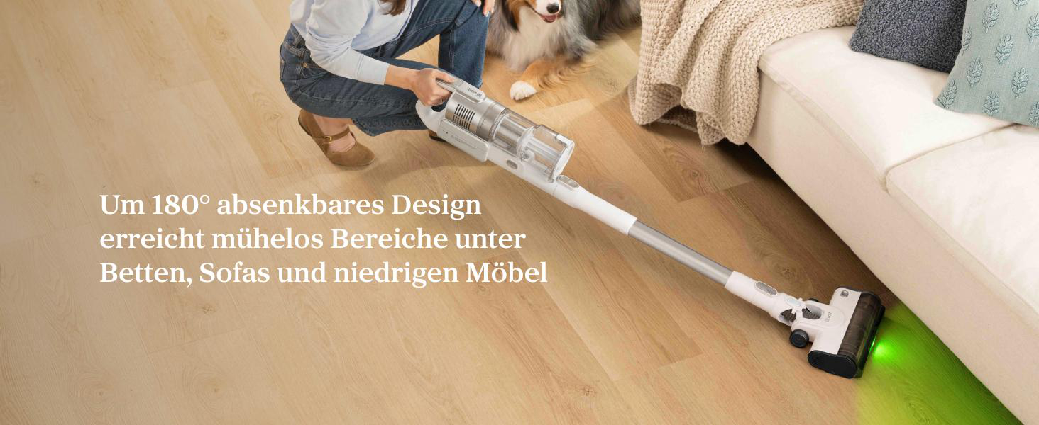 Person saugt mit weißem Staubsauger unter dem Sofa auf einem Holzboden.