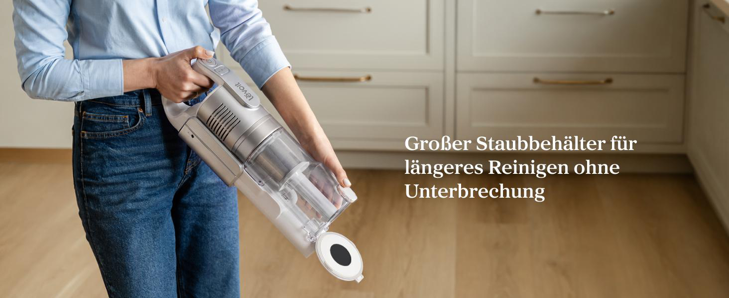 Eine Person hält einen Akku-Handstaubsauger mit geöffnetem Staubbehälter in einer Küche.