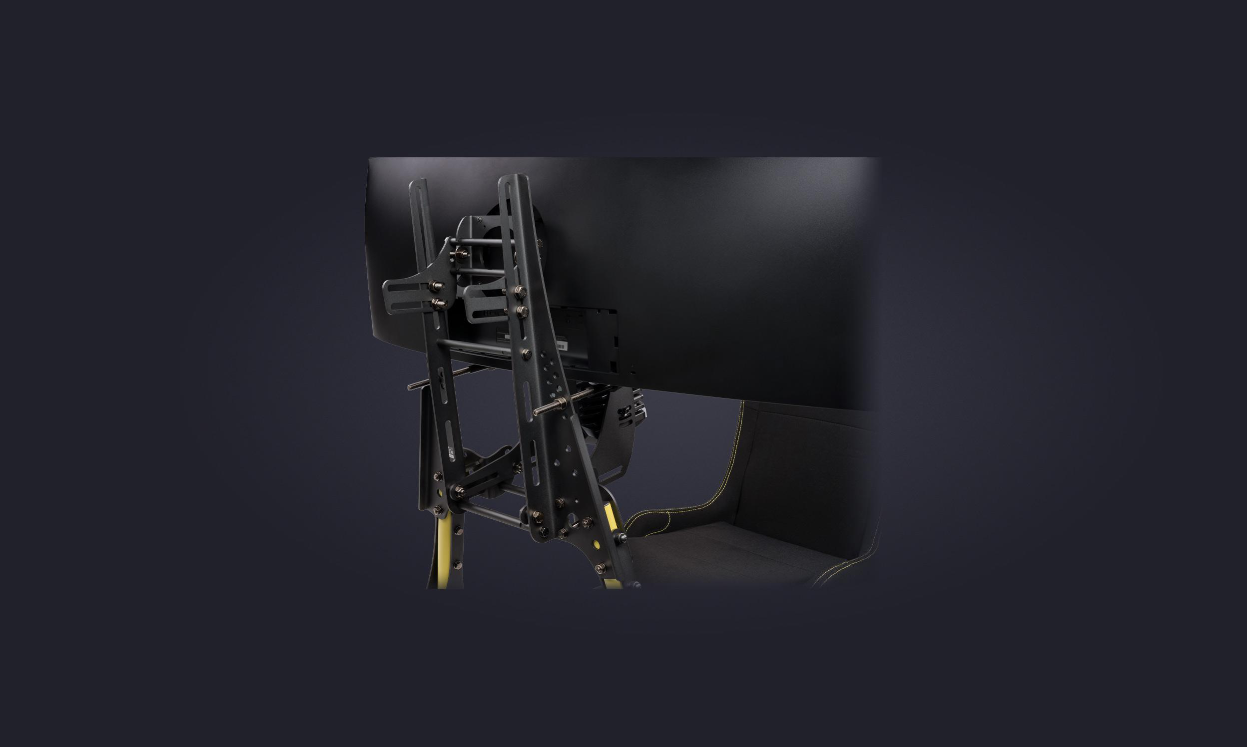 Rückseite eines großen Monitors, der an einer stabilen, schwarzen Metallhalterung über einem Gaming-Sitz befestigt ist.