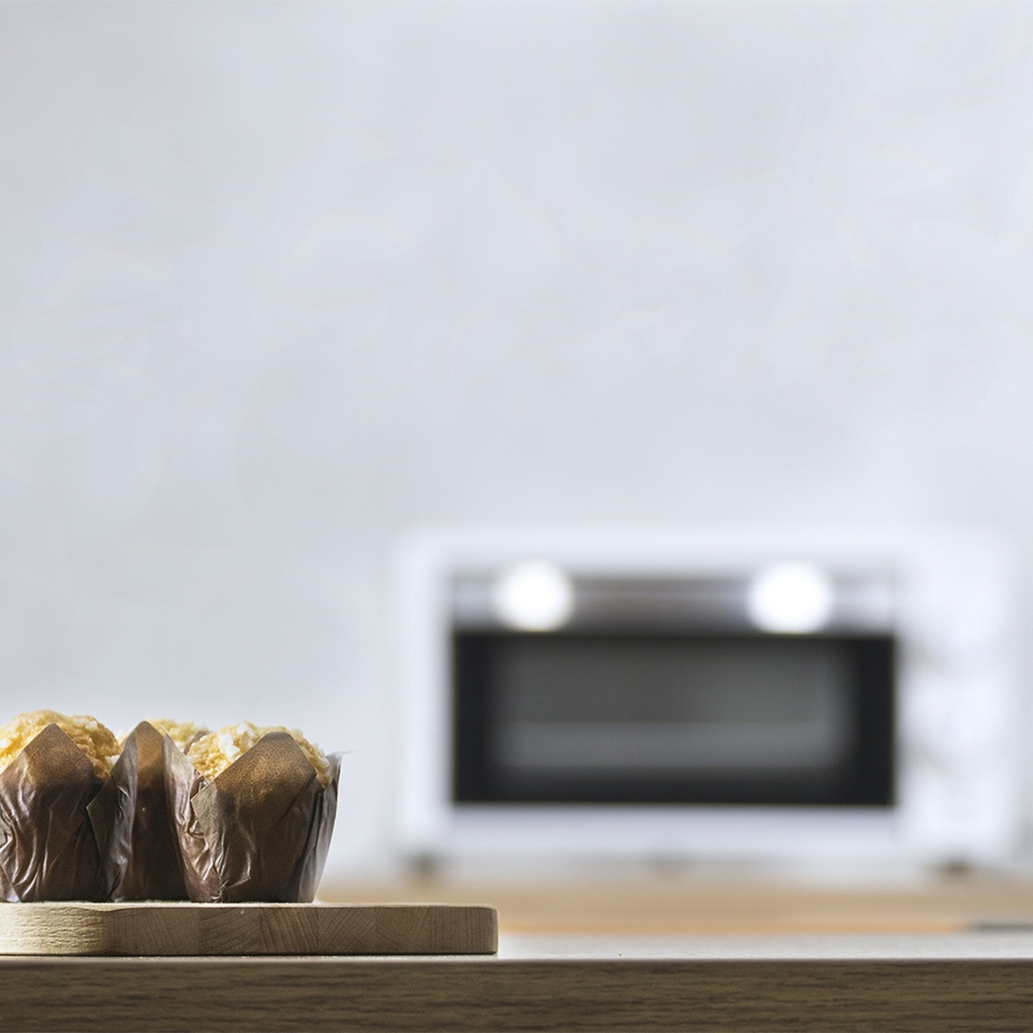 Tre muffin in pirottini marroni su un asse di legno davanti a un forno.