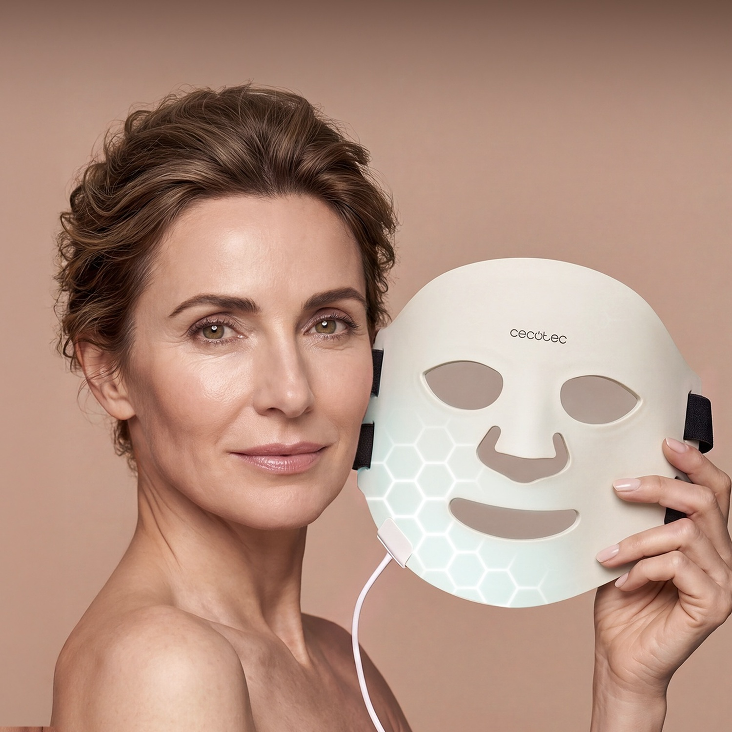 Una donna tiene una maschera facciale LED bianca con motivo vicino al viso.