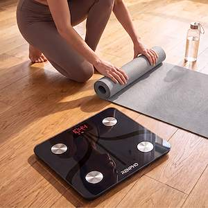 Una mujer desenrolla una esterilla de yoga en un suelo de madera mientras una báscula digital está en primer plano.