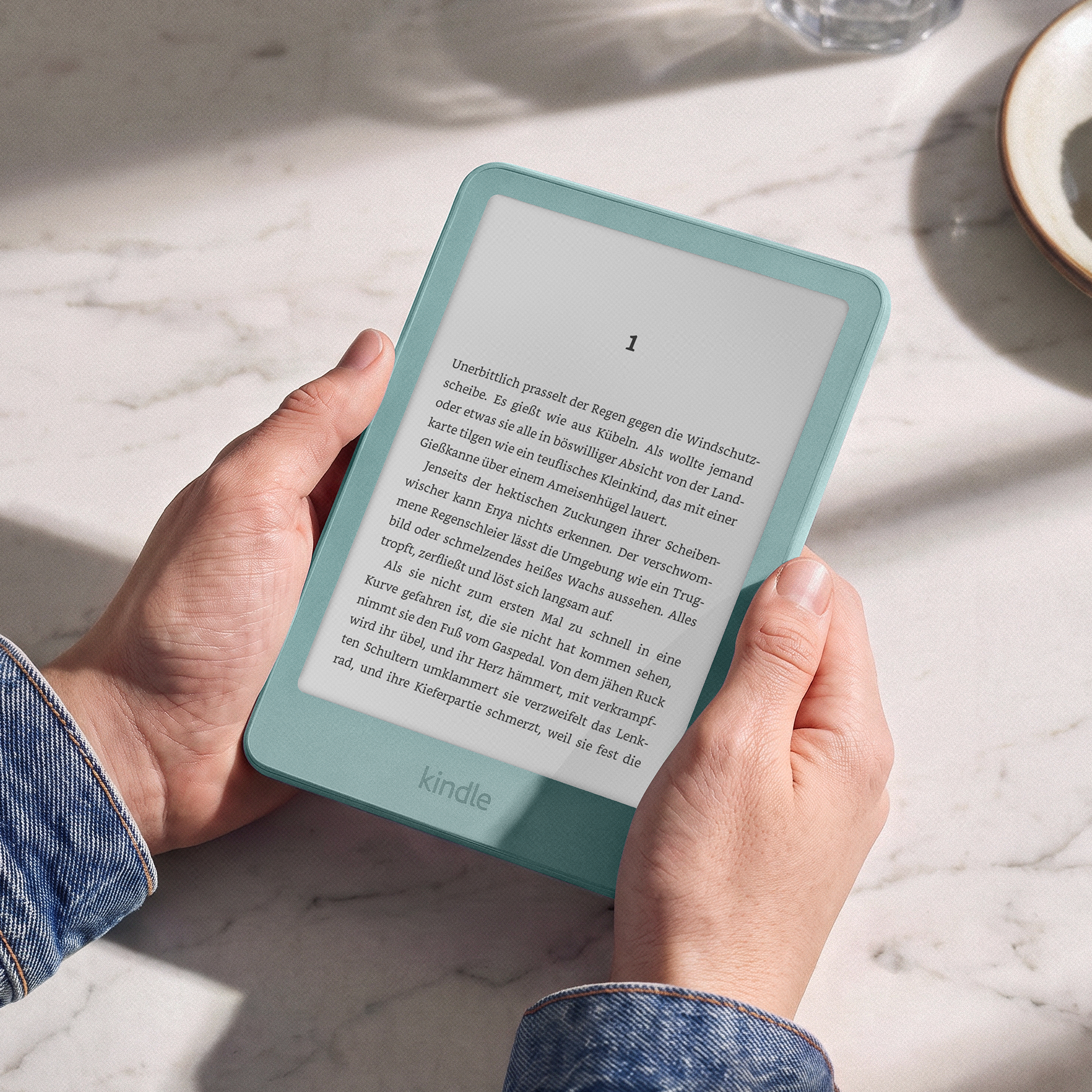 Person hält ein mintgrünes Kindle E-Reader mit offenem Buchtext auf einer Marmoroberfläche.