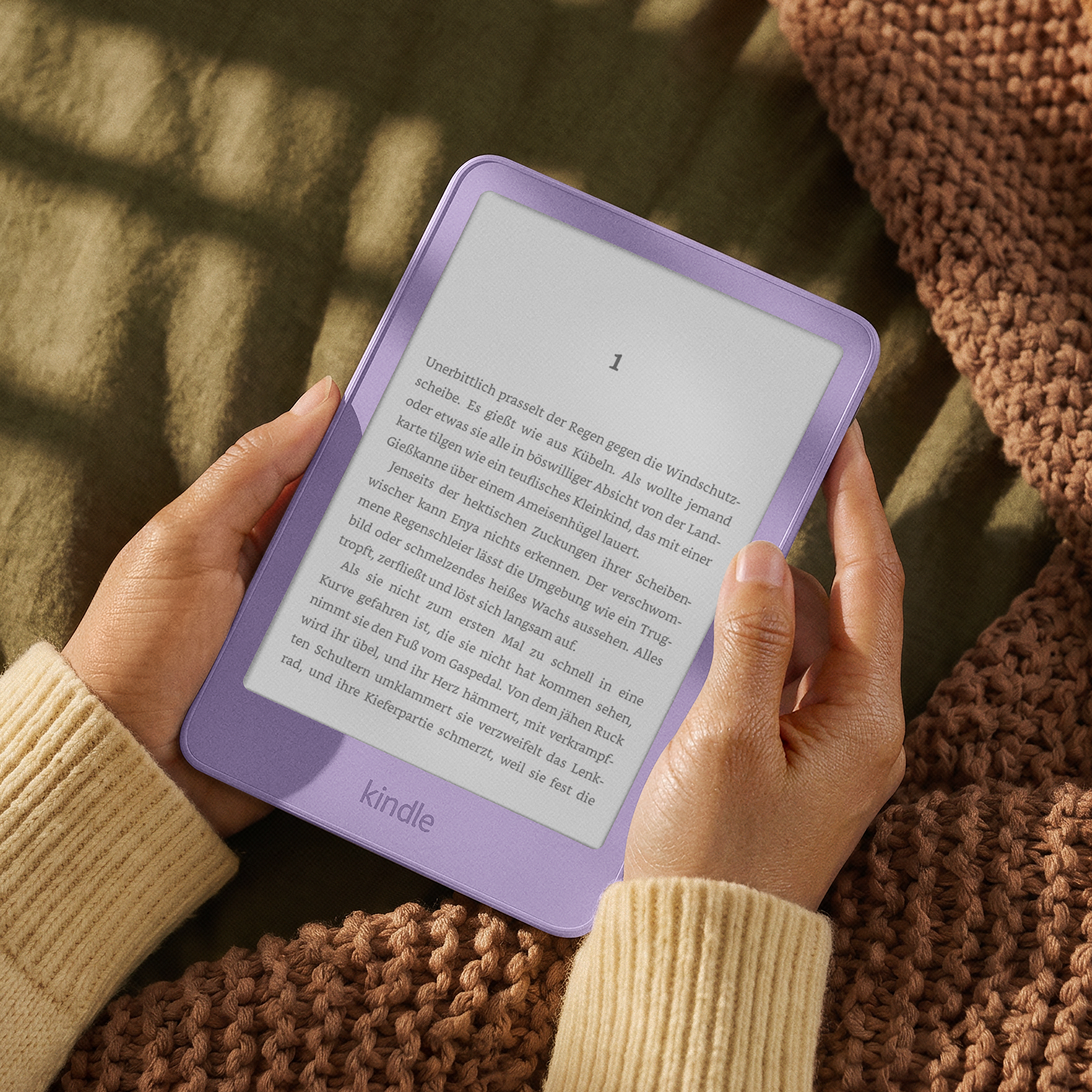 Eine Person hält einen hellvioletten Kindle-E-Reader mit deutschem Text auf dem Bildschirm auf einer Decke.