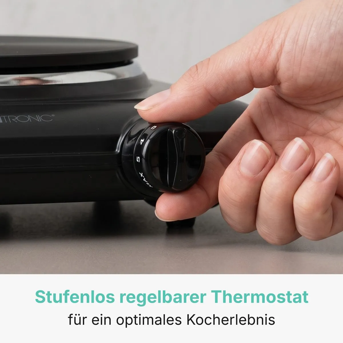 Eine Hand verstellt den runden Thermostatregler an einer schwarzen Elektrokochplatte.