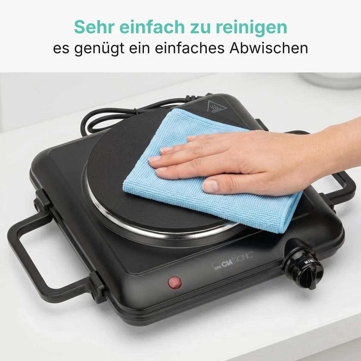 Eine Hand wischt mit einem blauen Tuch eine schwarze, tragbare Kochplatte ab.
