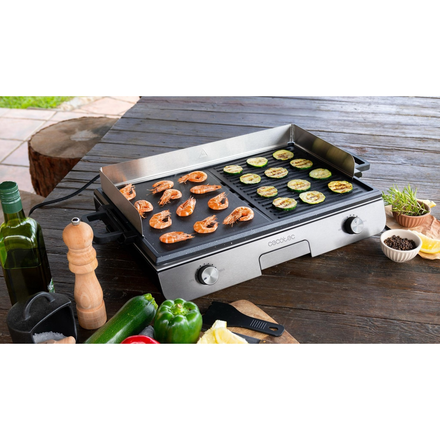 Una piastra elettrica su un tavolo di legno con gamberi, zucchine, olio e peperoni.