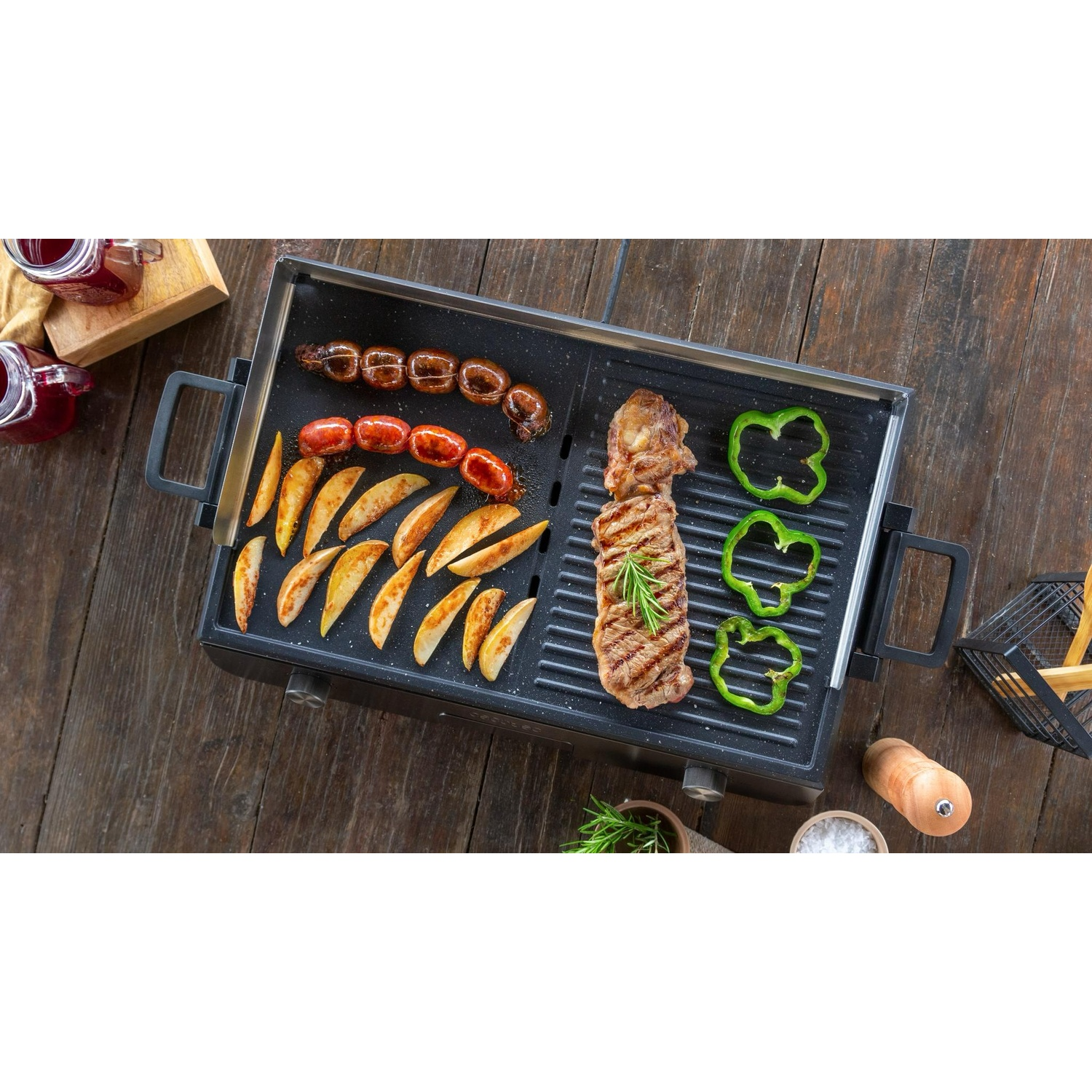 Una griglia elettrica su legno con carne, patate a spicchi e peperoni verdi.