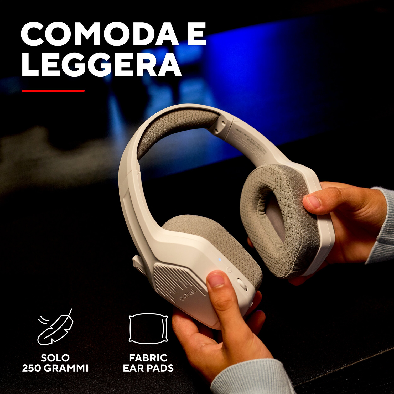 Mani tengono cuffie bianche over-ear con cuscinetti in tessuto su sfondo scuro.