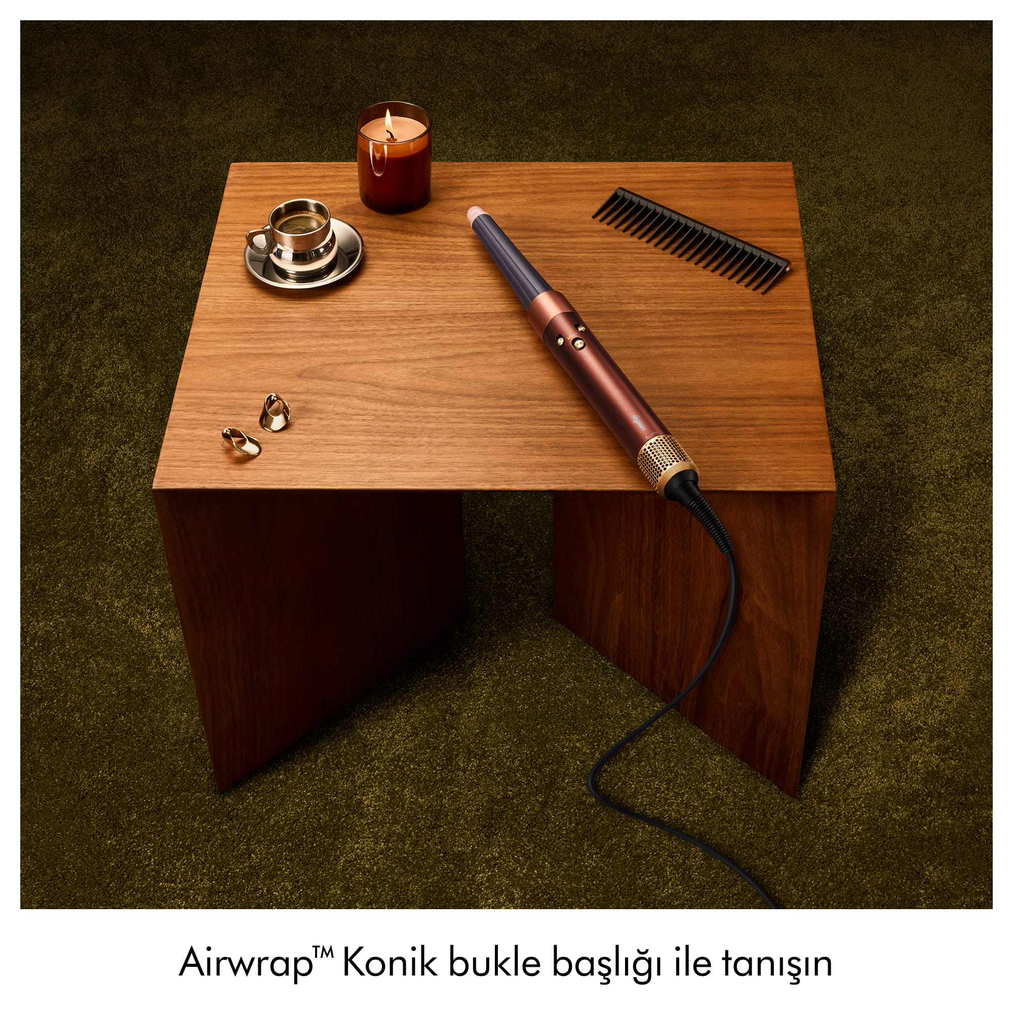 Yeşil halı üzerinde ahşap sehpa, maşa, kahve fincanı, mum, tarak ve küpeler içeriyor.