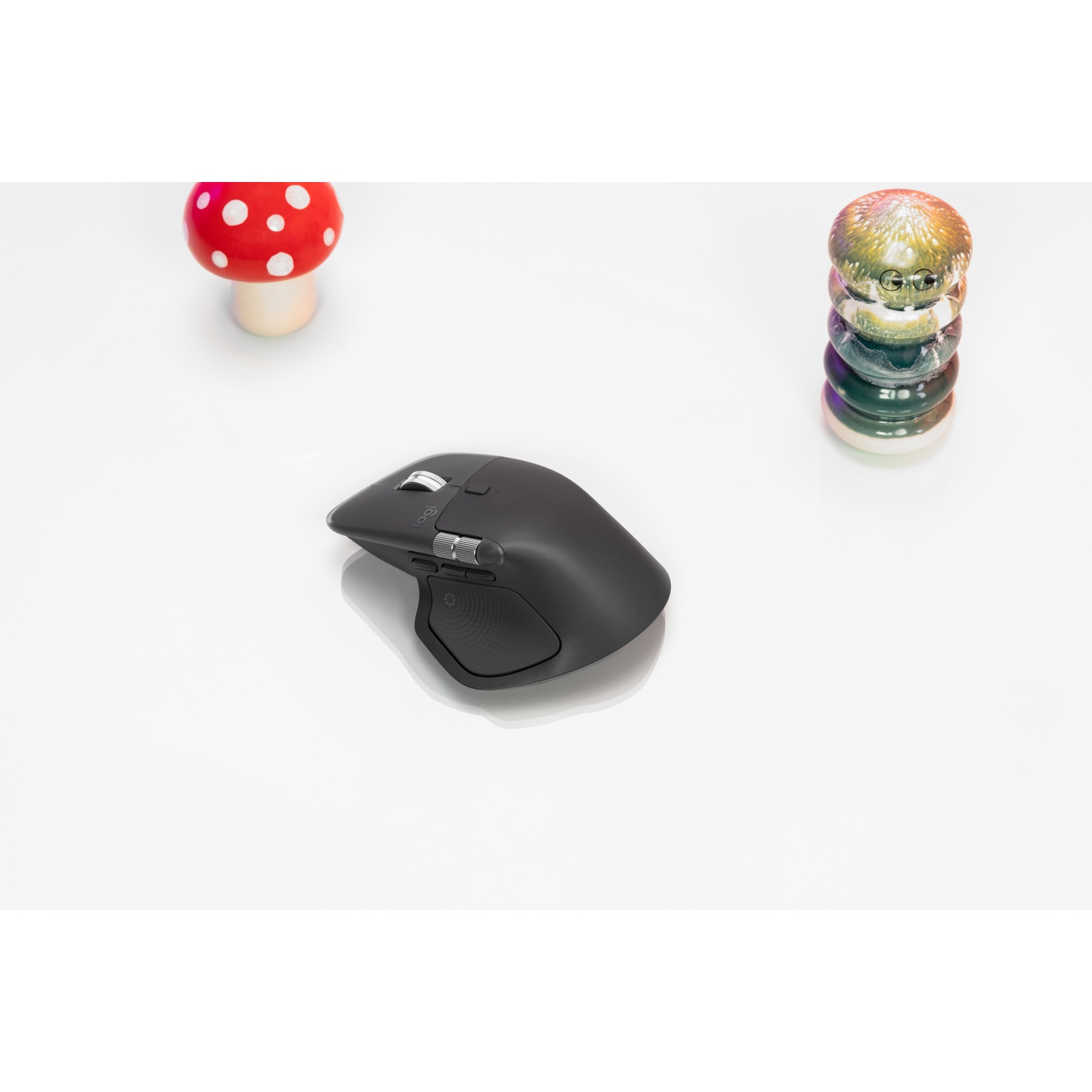 Un mouse per computer nero su sfondo bianco, affiancato da un fungo rosso e da una colorata figura decorativa.