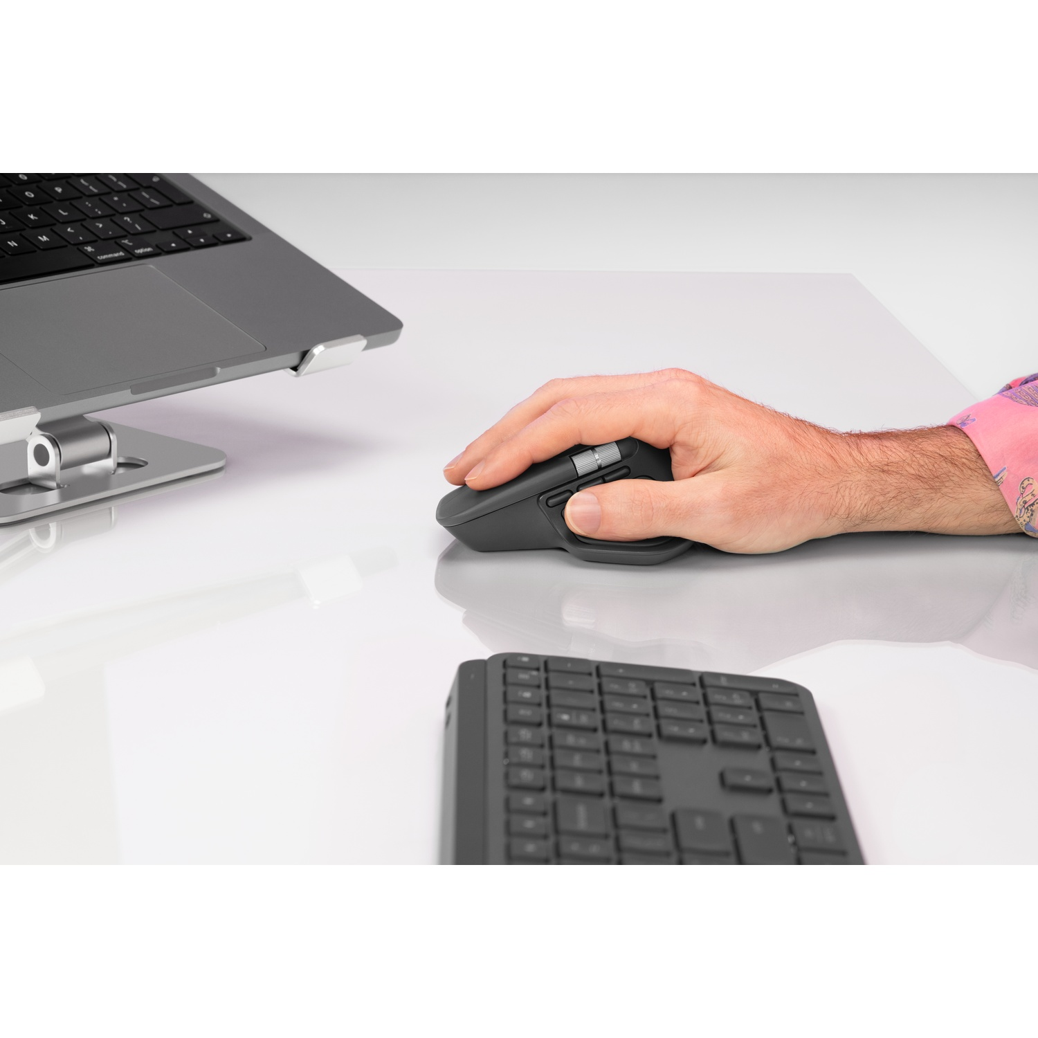 Una mano usa un mouse per computer grigio su una scrivania bianca accanto a un computer portatile.