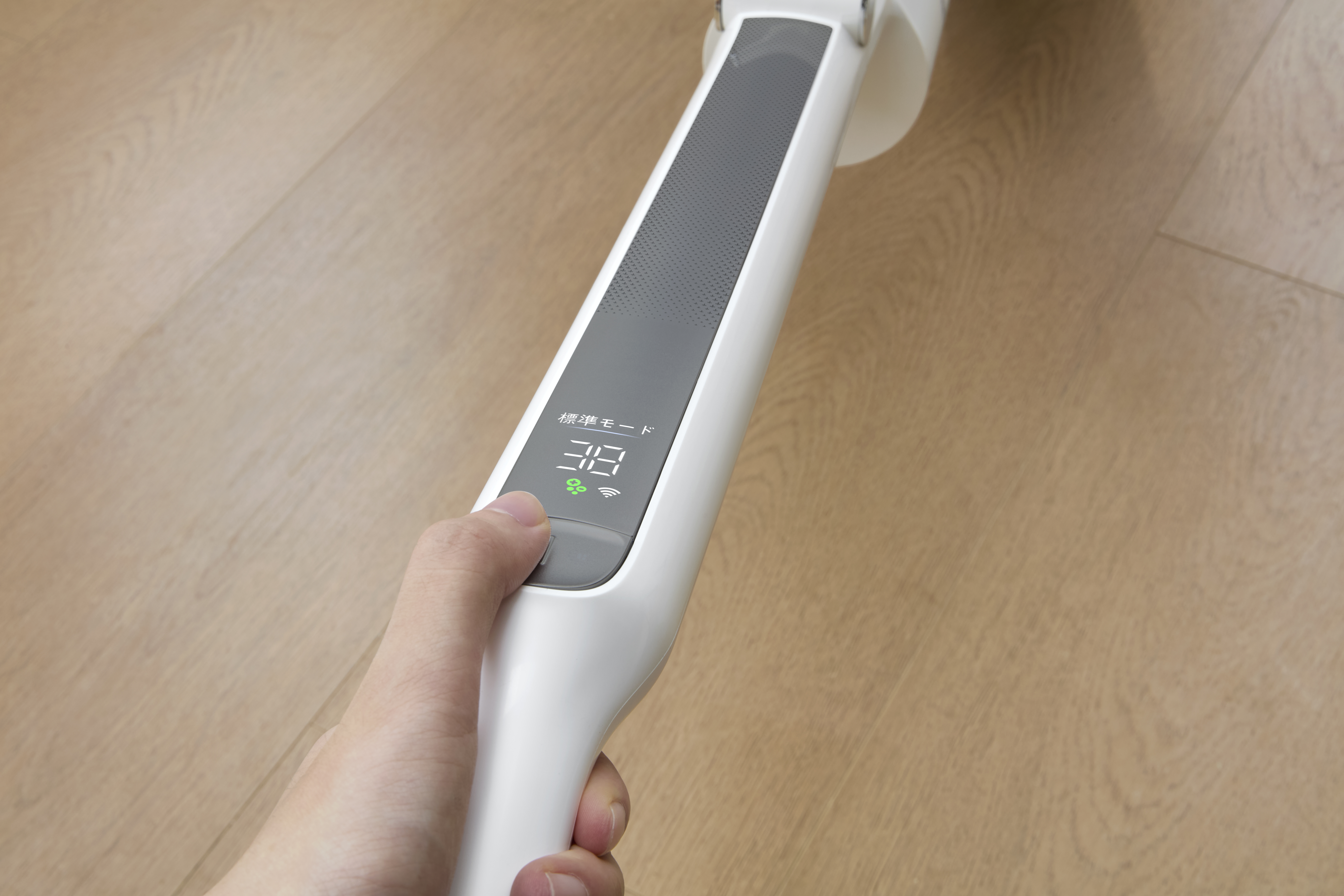 Hand hält weißes elektronisches Gerät mit digitalem Display und Text über Holzboden.