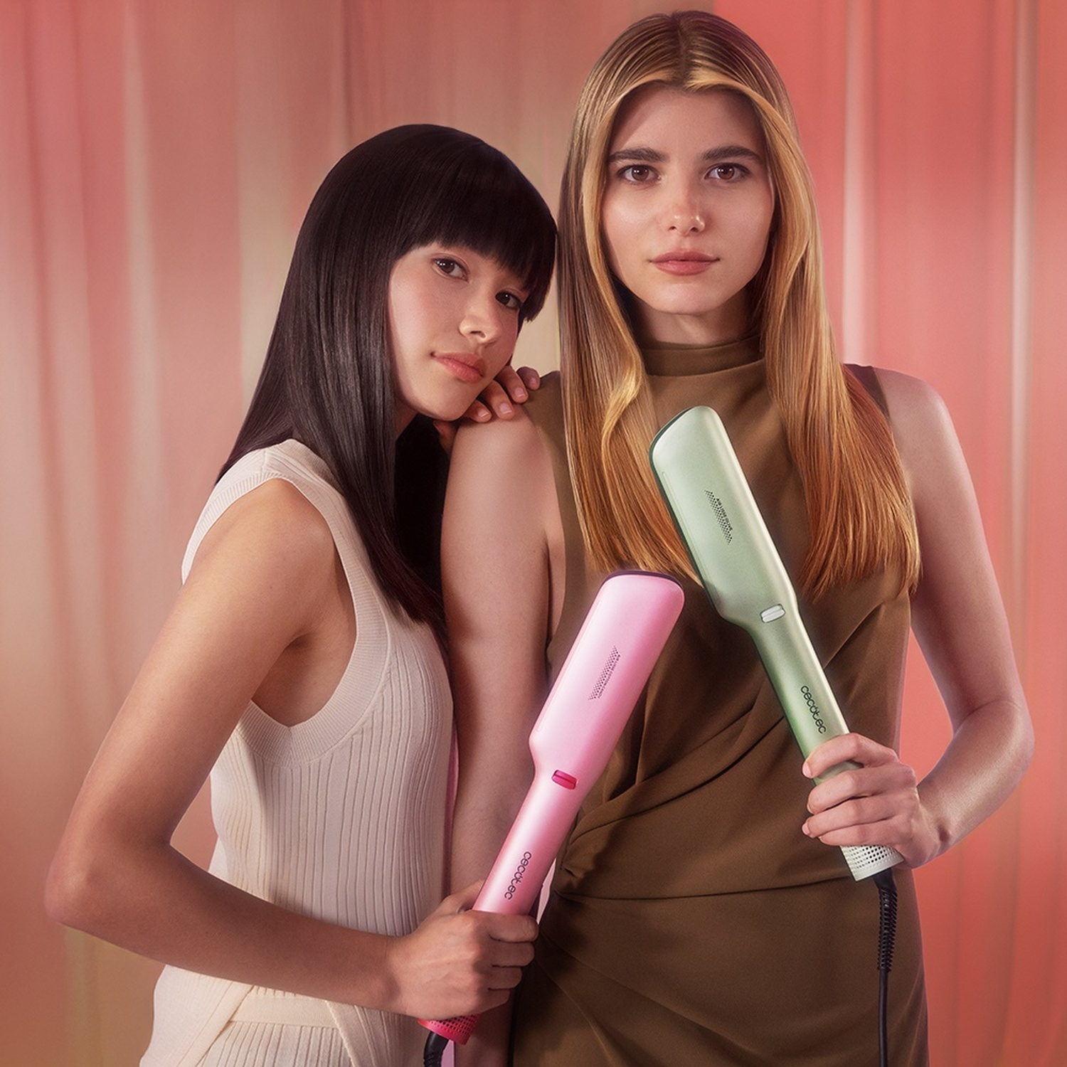 Due donne tengono piastre per capelli rosa e verde chiaro su sfondo rosa.