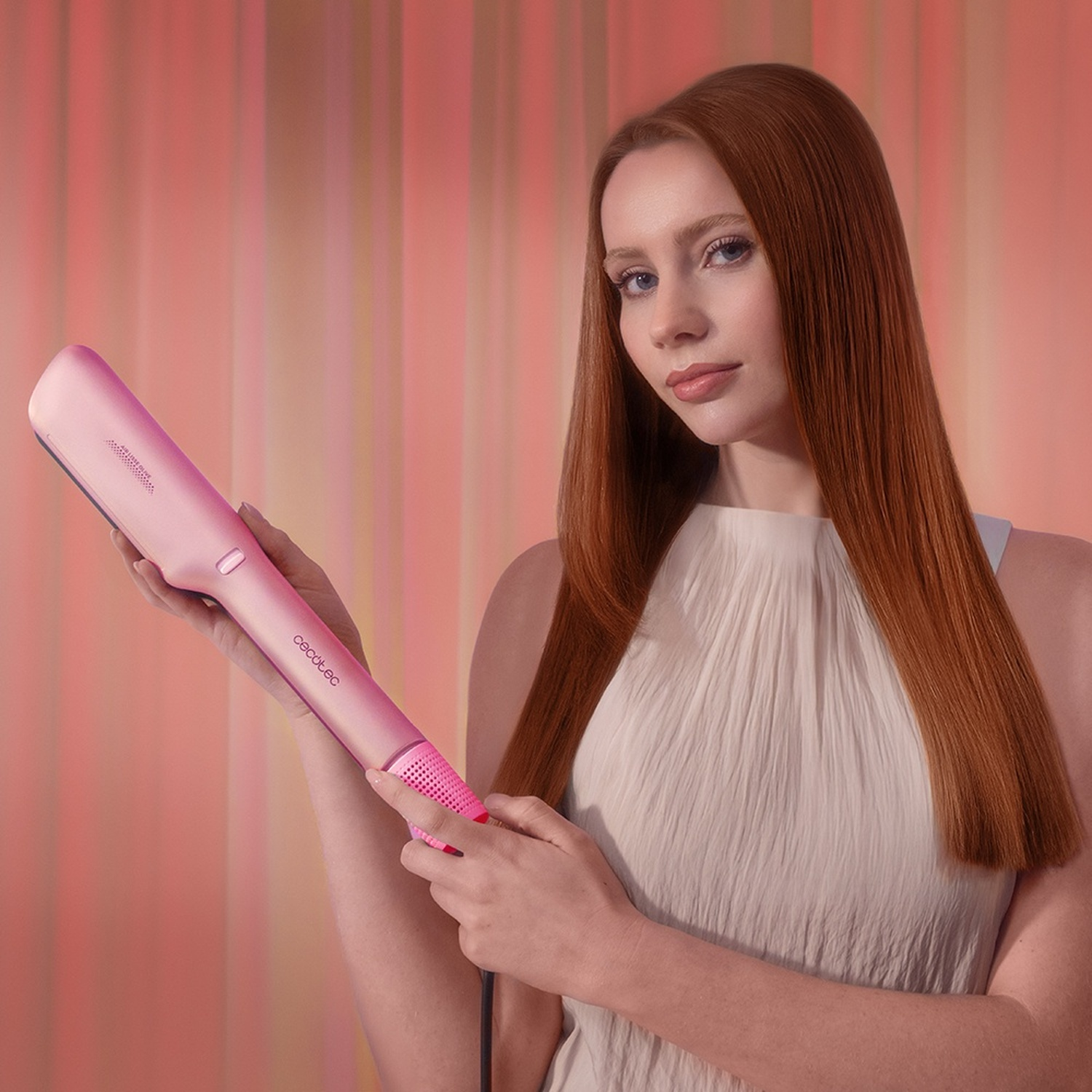 Donna dai capelli rossi tiene una piastra per capelli rosa su sfondo a righe.
