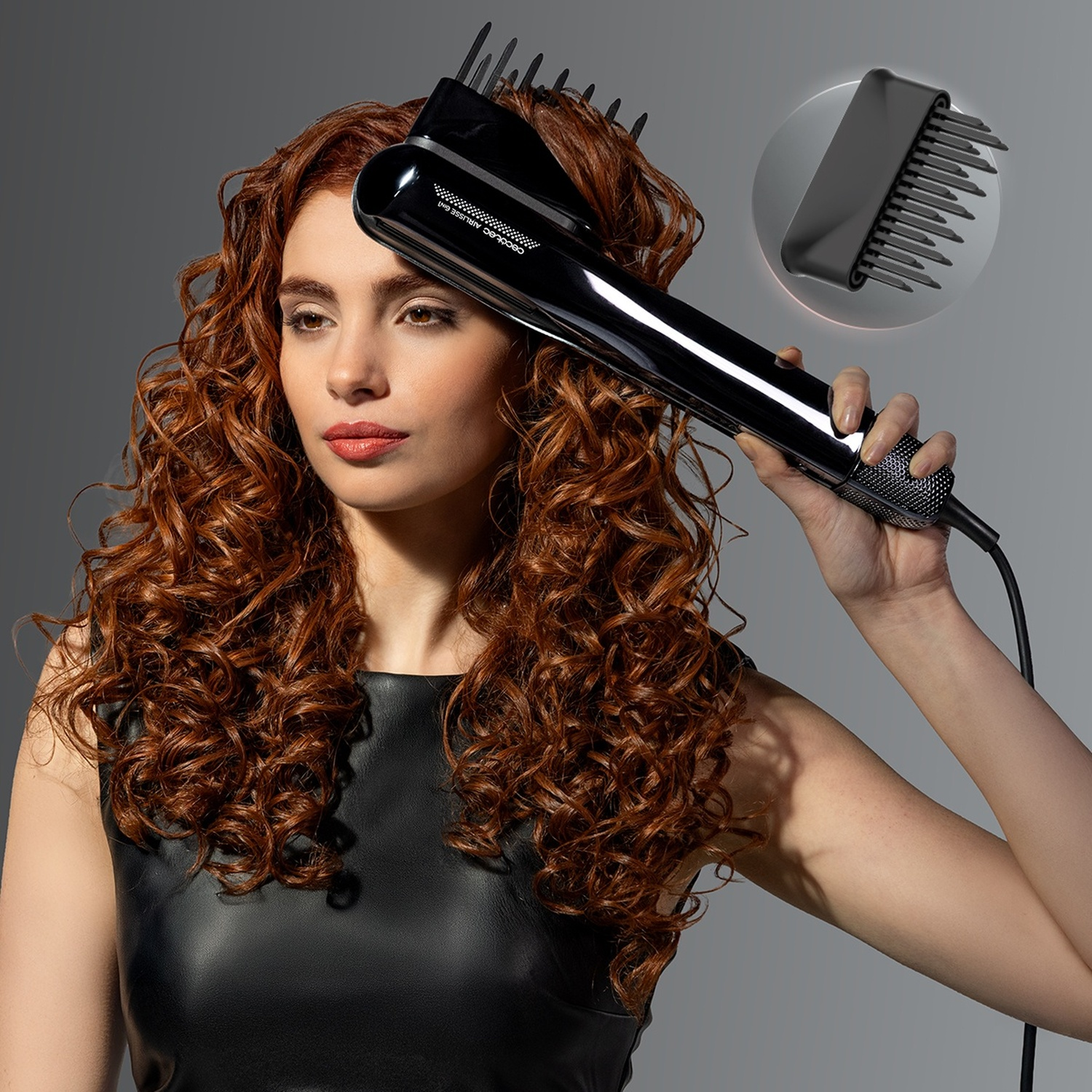 Una donna con lunghi capelli rossi ricci modella i capelli con uno styler nero su sfondo grigio.
